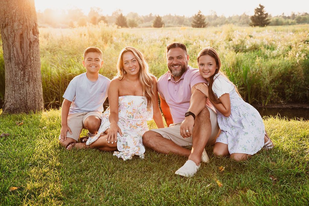 Family photo session outdoors with warm sunset lighting in grassy field.