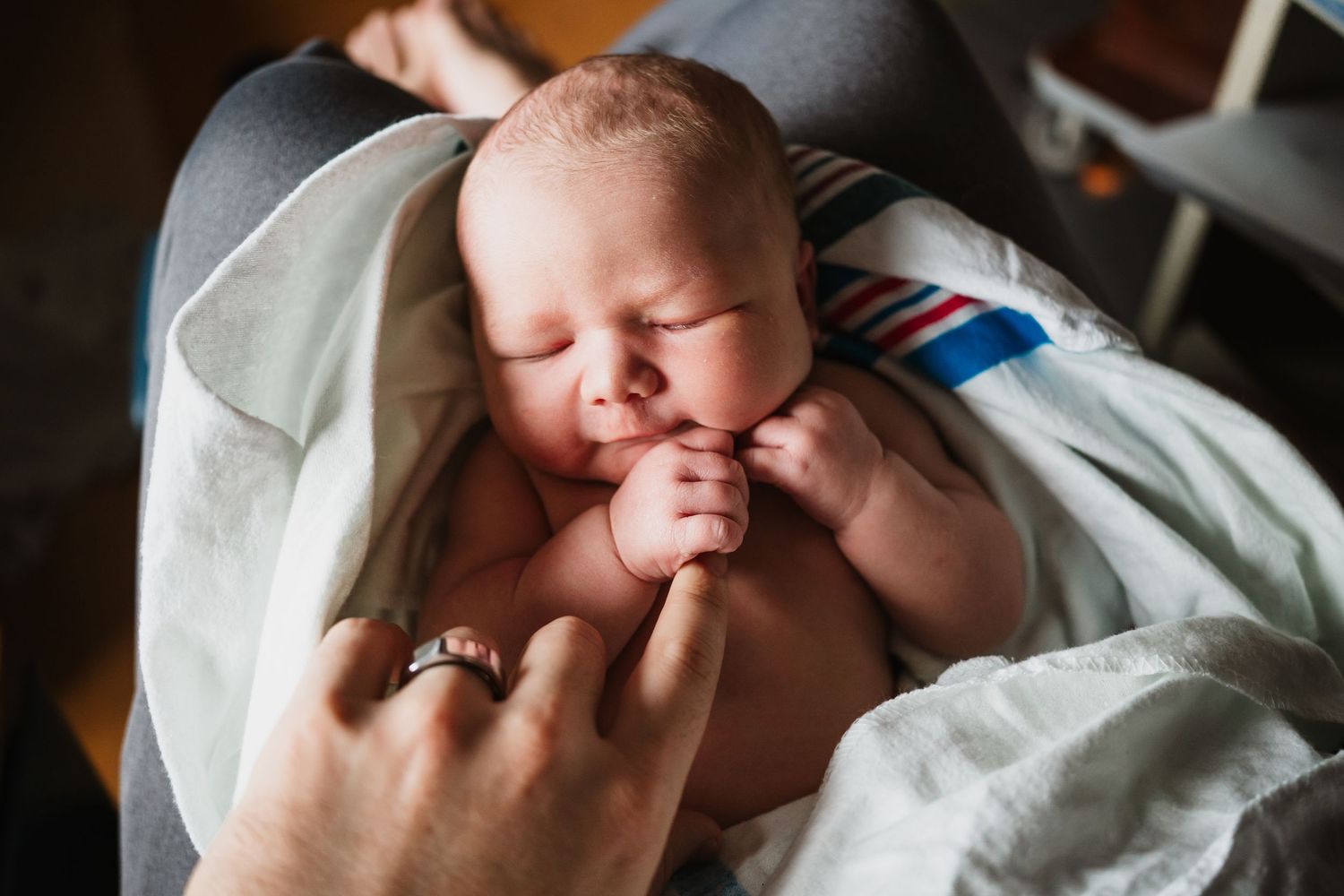 Newborn baby sleeping peacefully wrapped in a white blanket, cradled in an adult's arms.