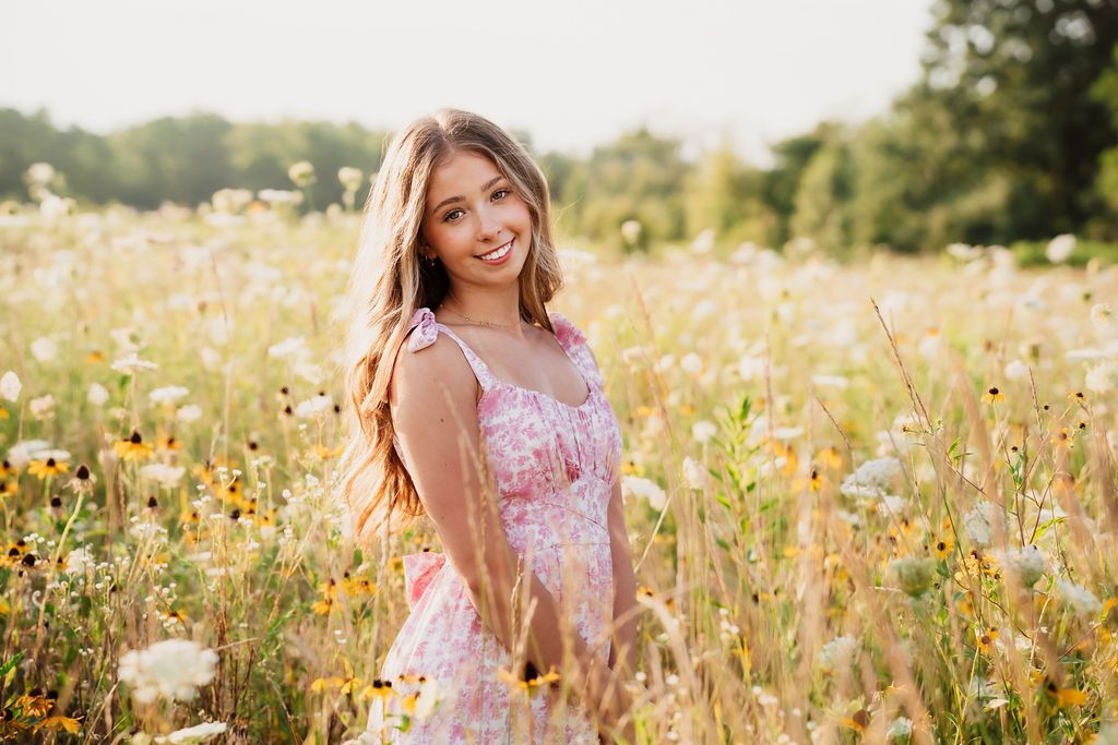 A person in a pink floral dress sits among vibrant yellow wildflowers in a sunny meadow during golden hour.