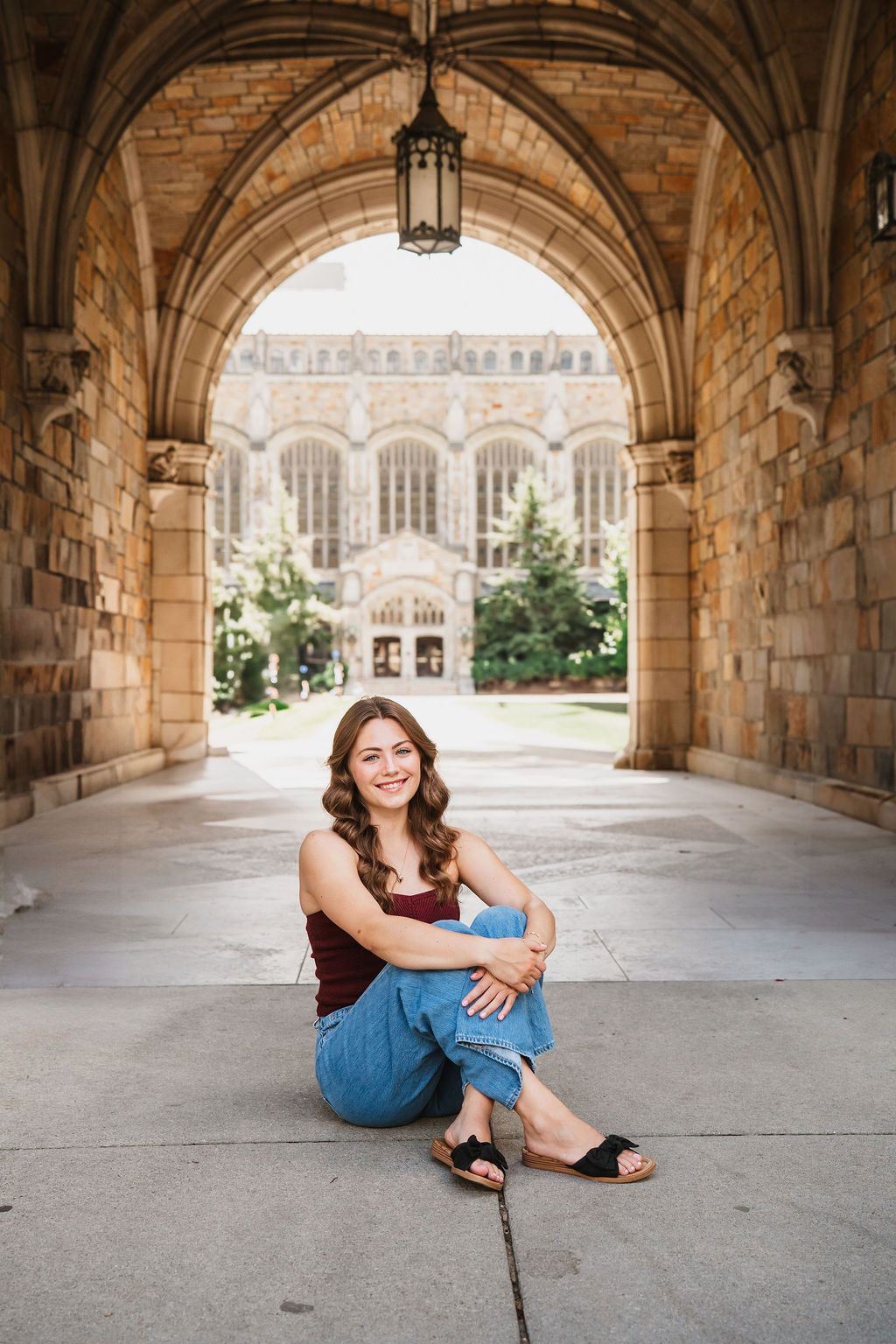 A student poses for a portrait under a Gothic stone archway at a university campus with collegiate architecture.