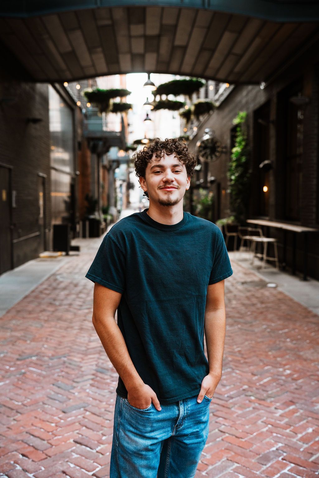 Person in casual blue outfit poses against brick wall backdrop in urban alleyway setting.
