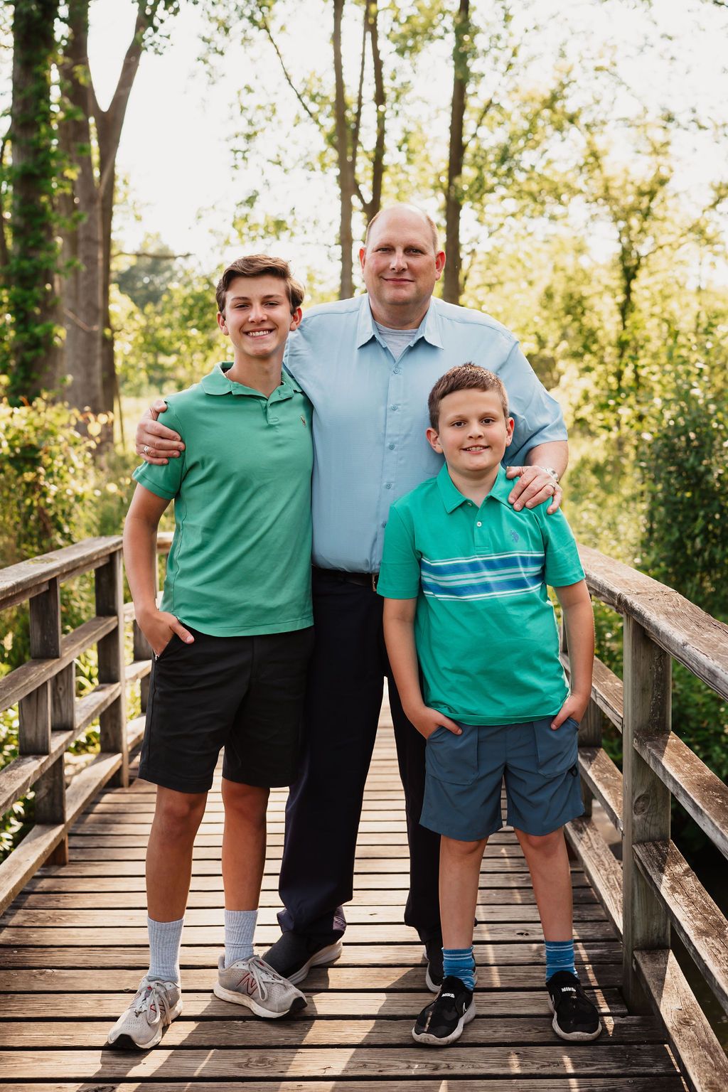 Family photos on a wooden bridge with coordinated green outfits in a park setting during golden hour.