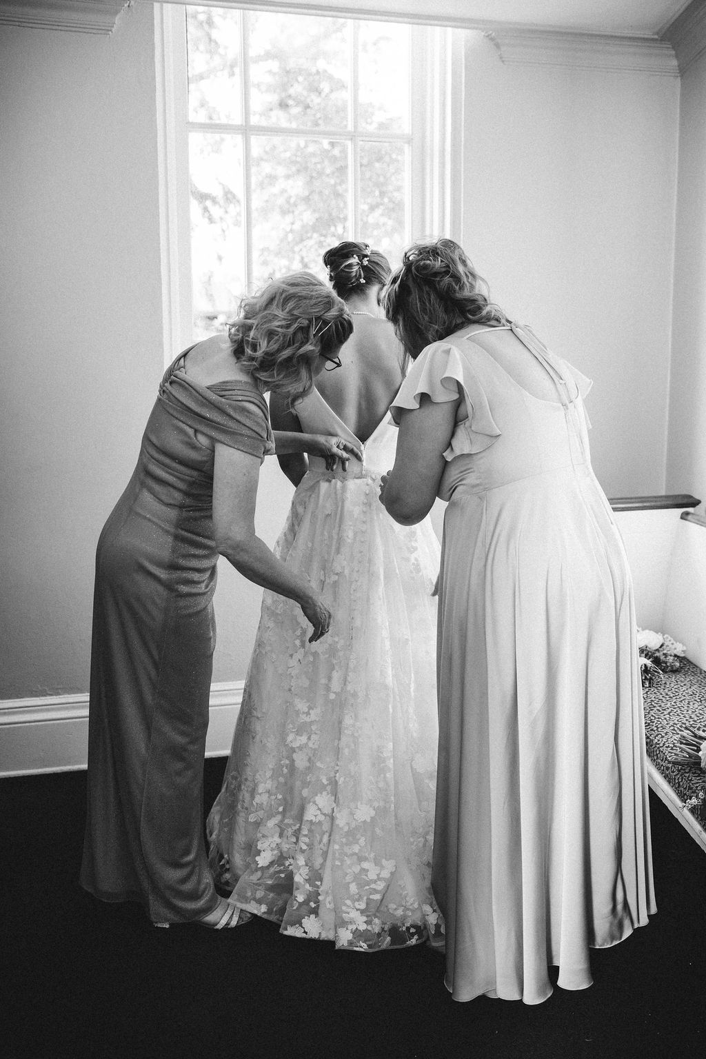 Black and white series showing preparations with white wedding dresses being adjusted and fitted.