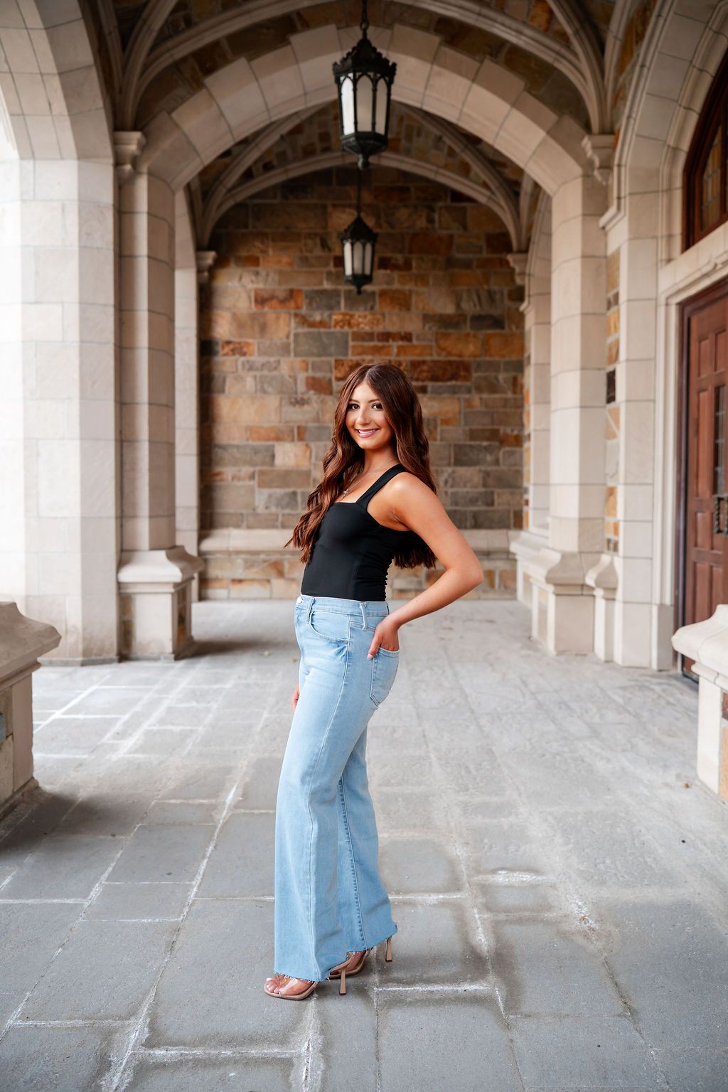 Person posing under stone archway wearing casual outfit with light denim jeans. University of Michigan law quad senior photos