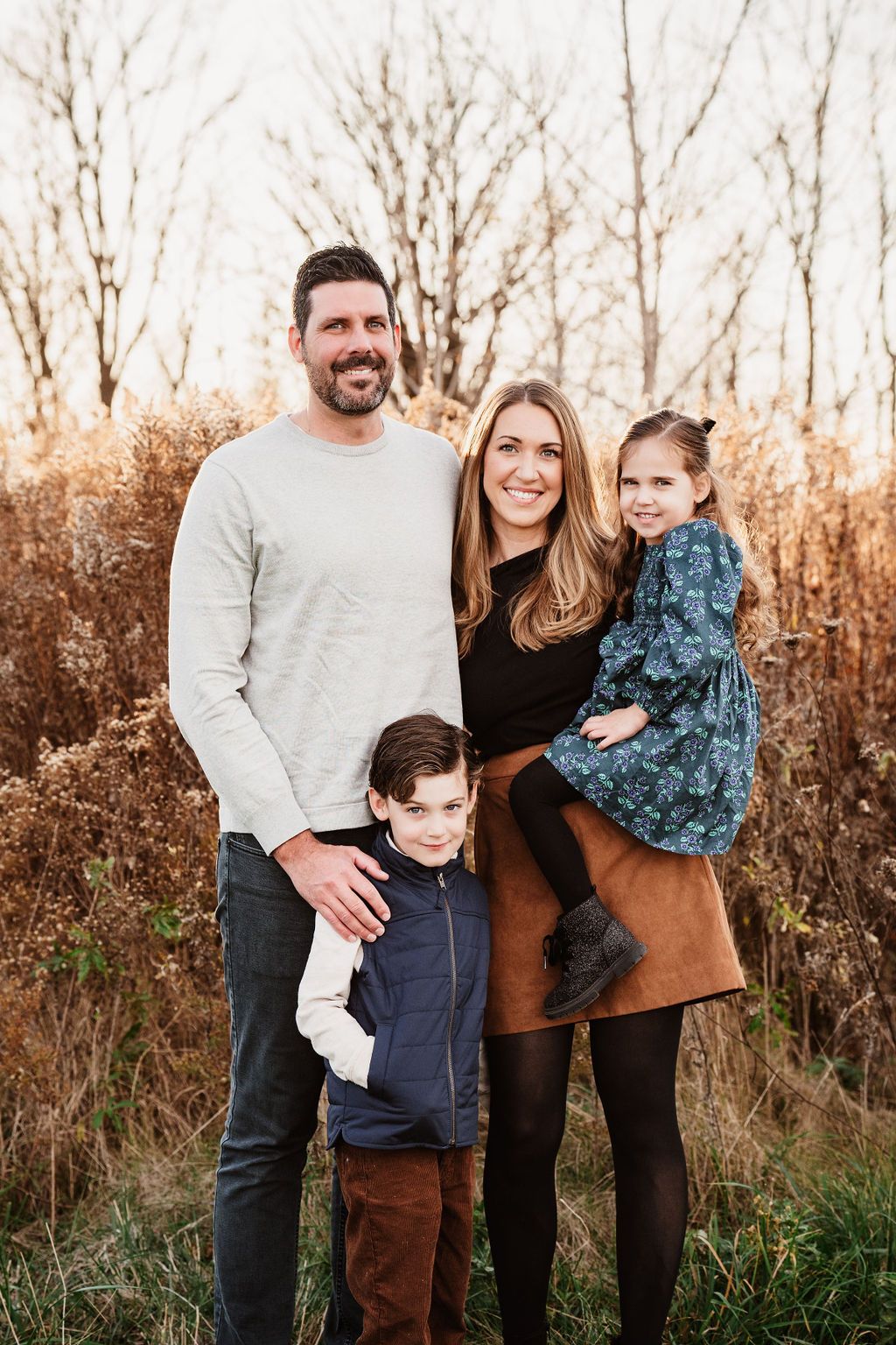 Family portrait session at sunset in a natural field setting with warm autumn colors.