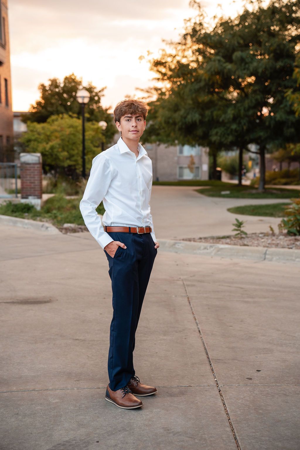 Teen boy in white dress shirt and navy pants standing outdoors at sunset.