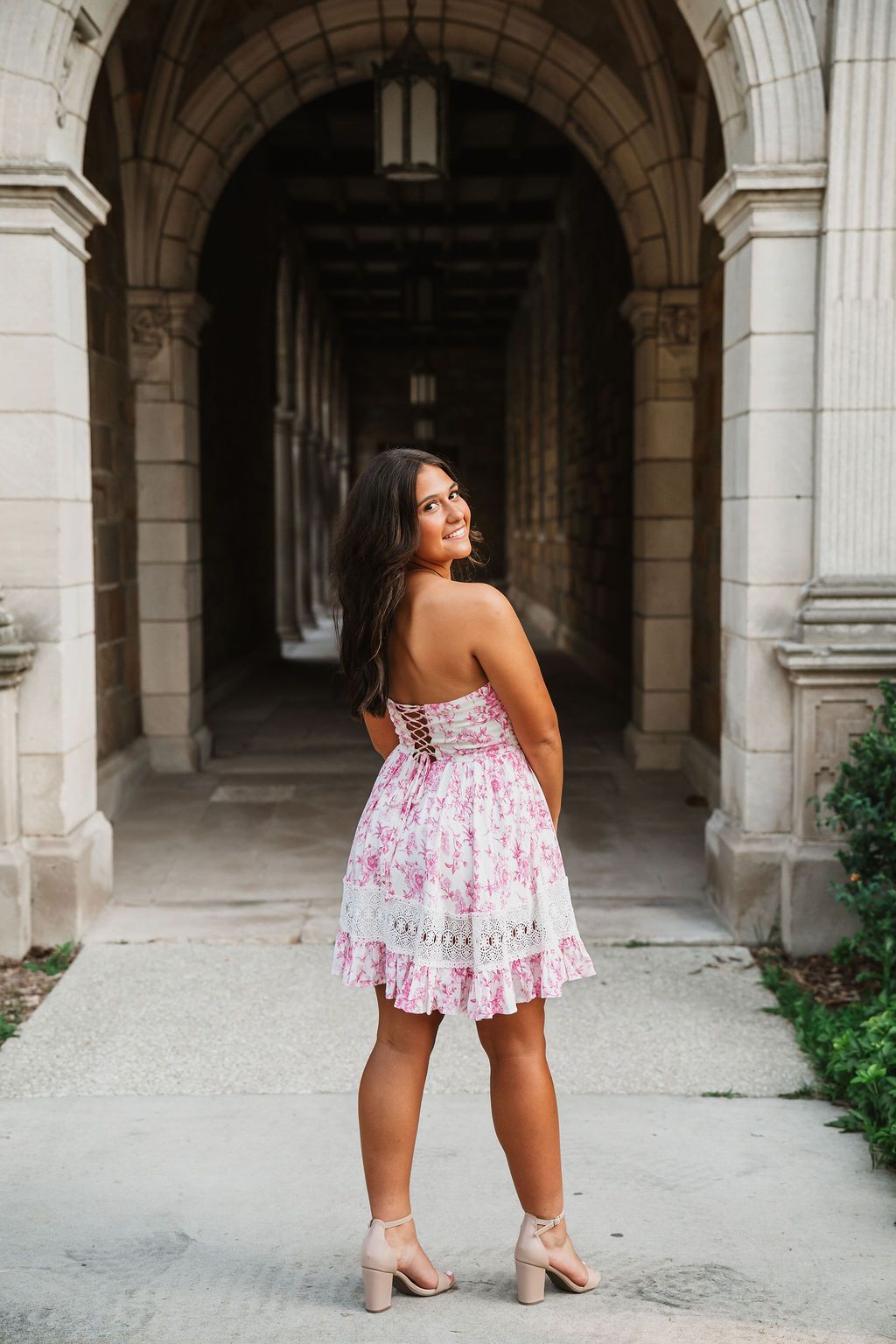 Person in floral dress poses in elegant stone archway corridor.