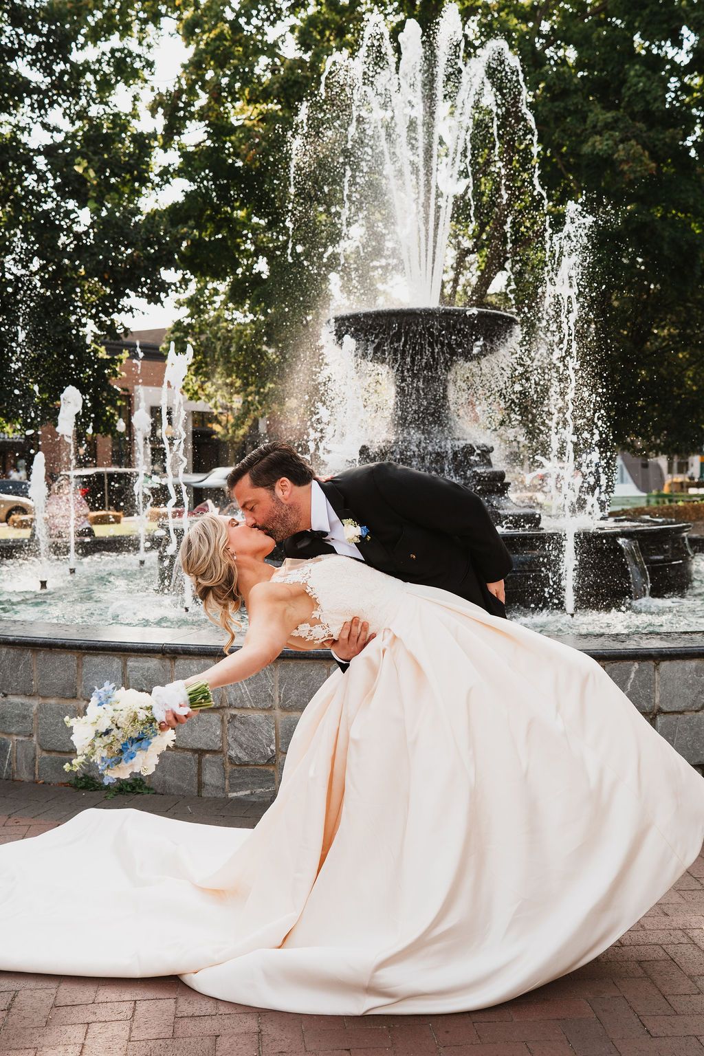 Romantic wedding couple posing by fountain with bride's dress flowing dramatically.