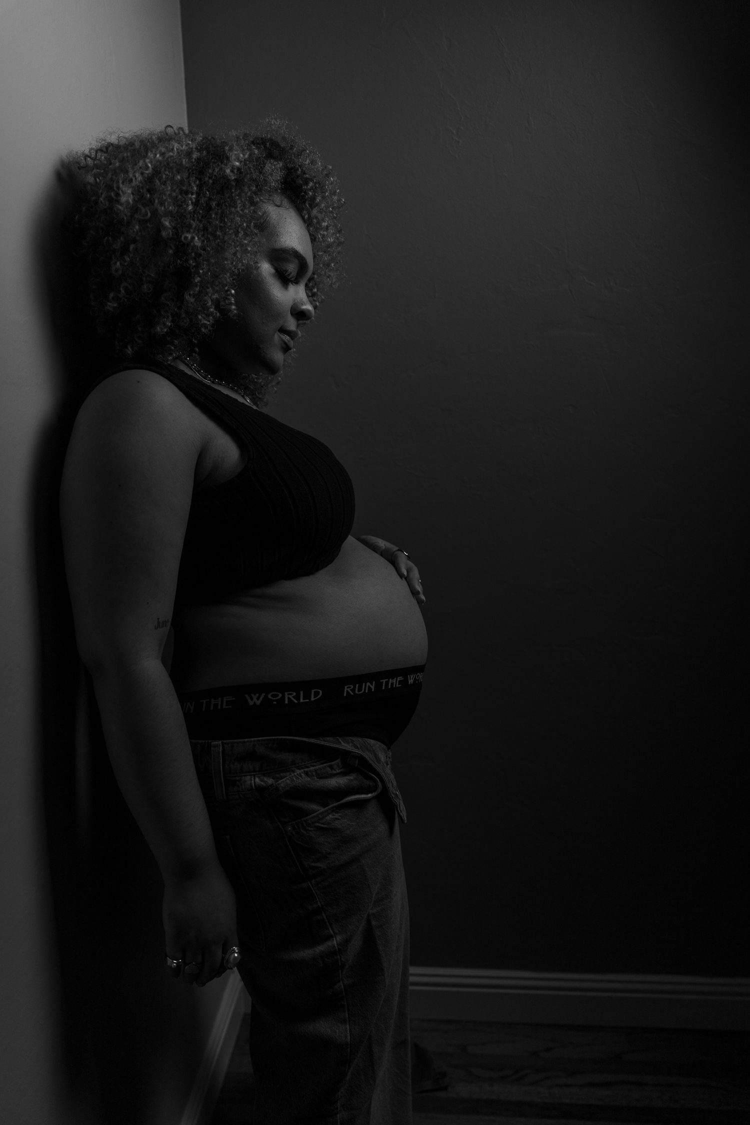 A profile series of a person with curly hair in black and white dramatic lighting wearing dark clothing against dark backdrop.