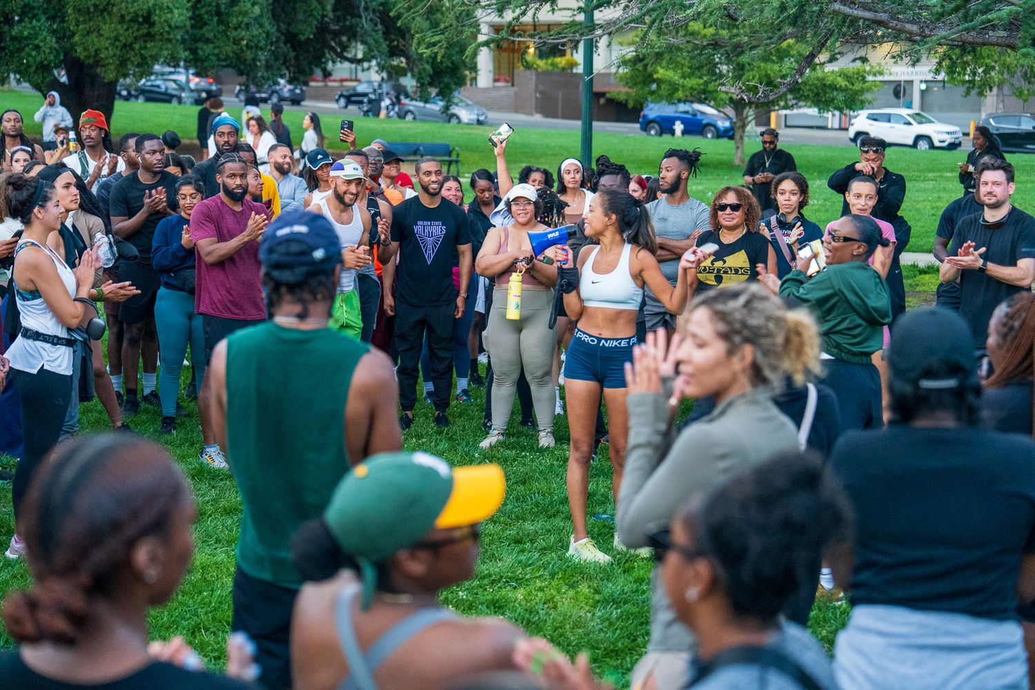 Large crowd gathered for an outdoor fitness event with green parkland in the background.