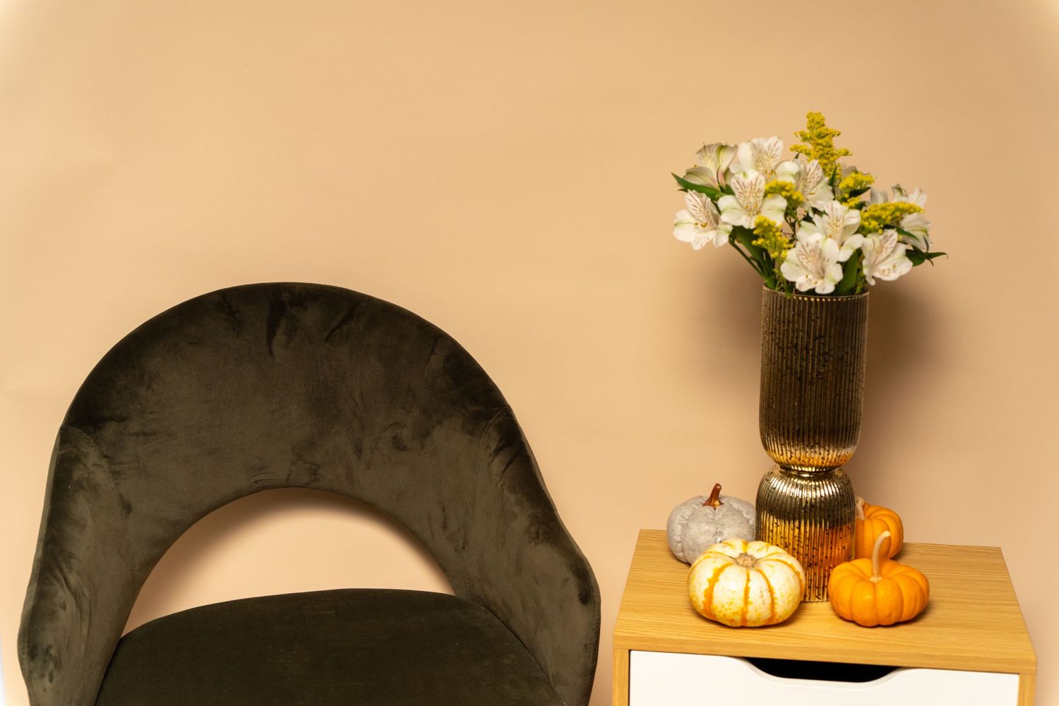 Studio setting with a green velvet chair and decorative elements on a beige background.