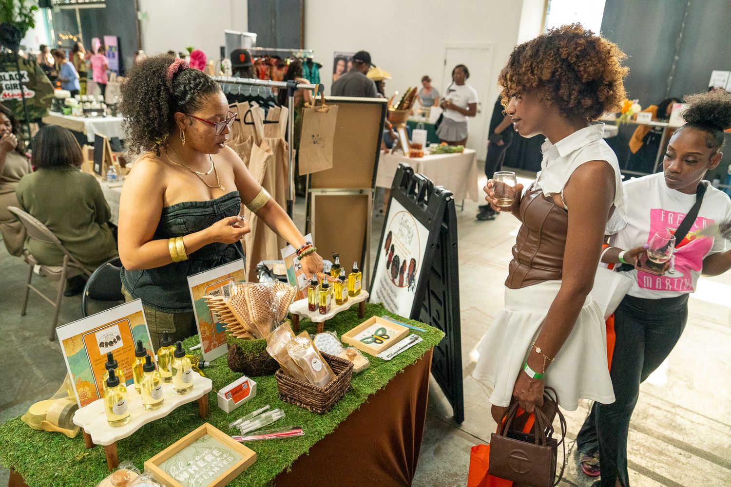 People explore vendor booths and displays at an indoor market event.