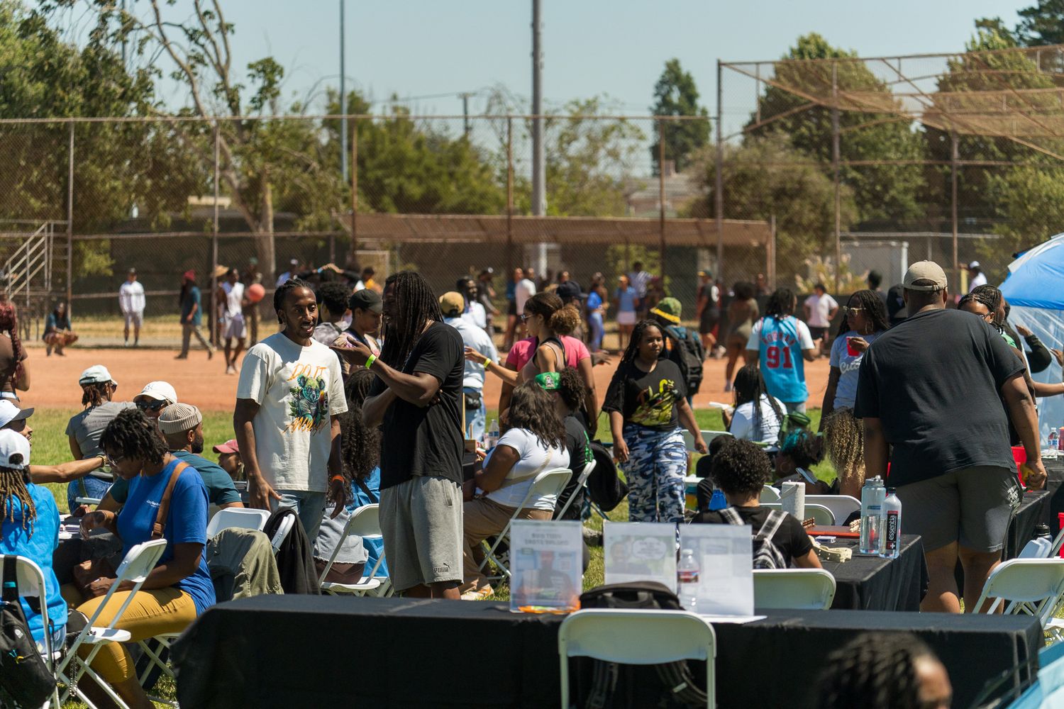 Large group of spectators watching an outdoor event with trees in the background.