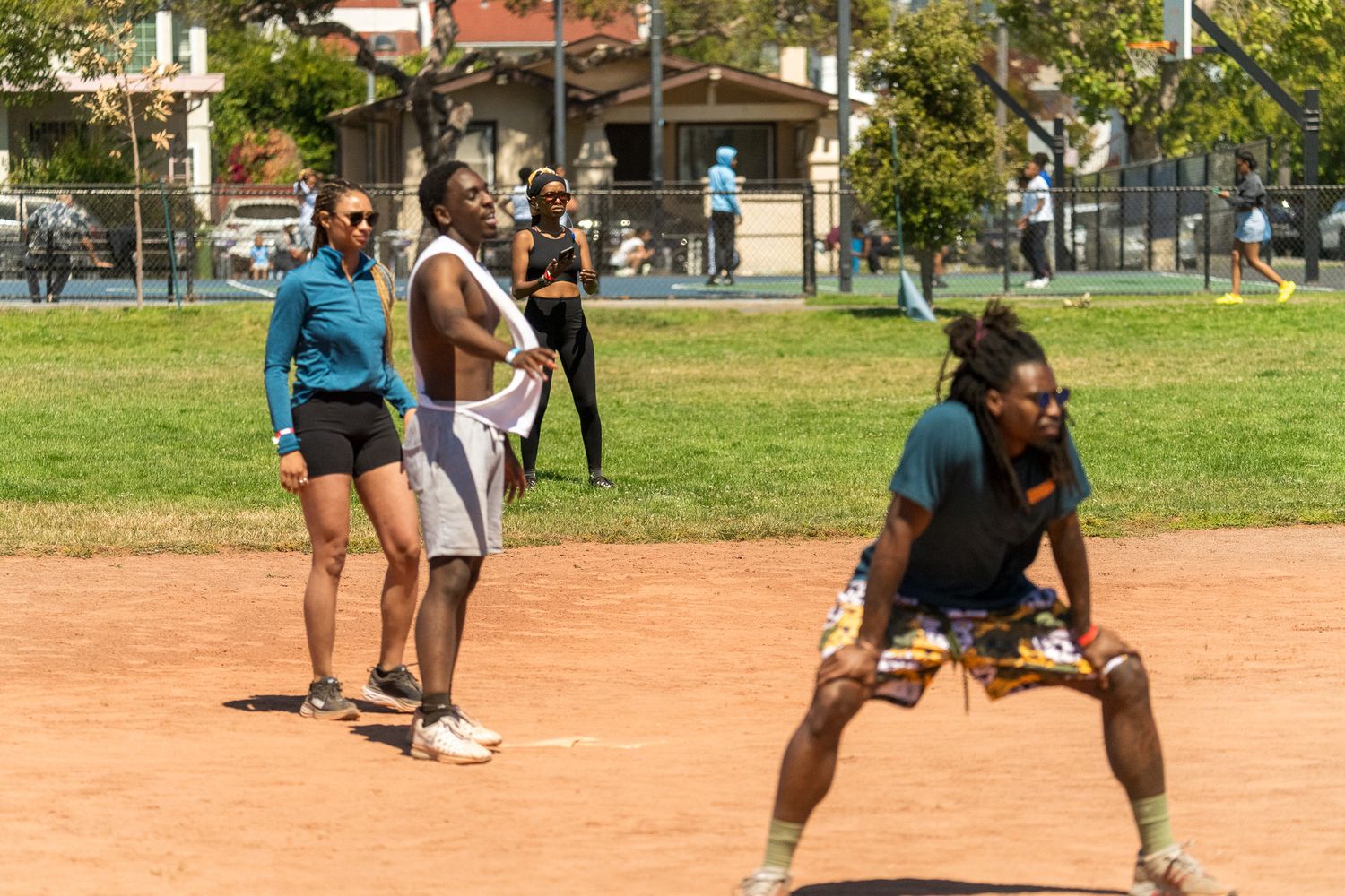 Players in athletic gear compete on a dirt sports field during a sunny day.