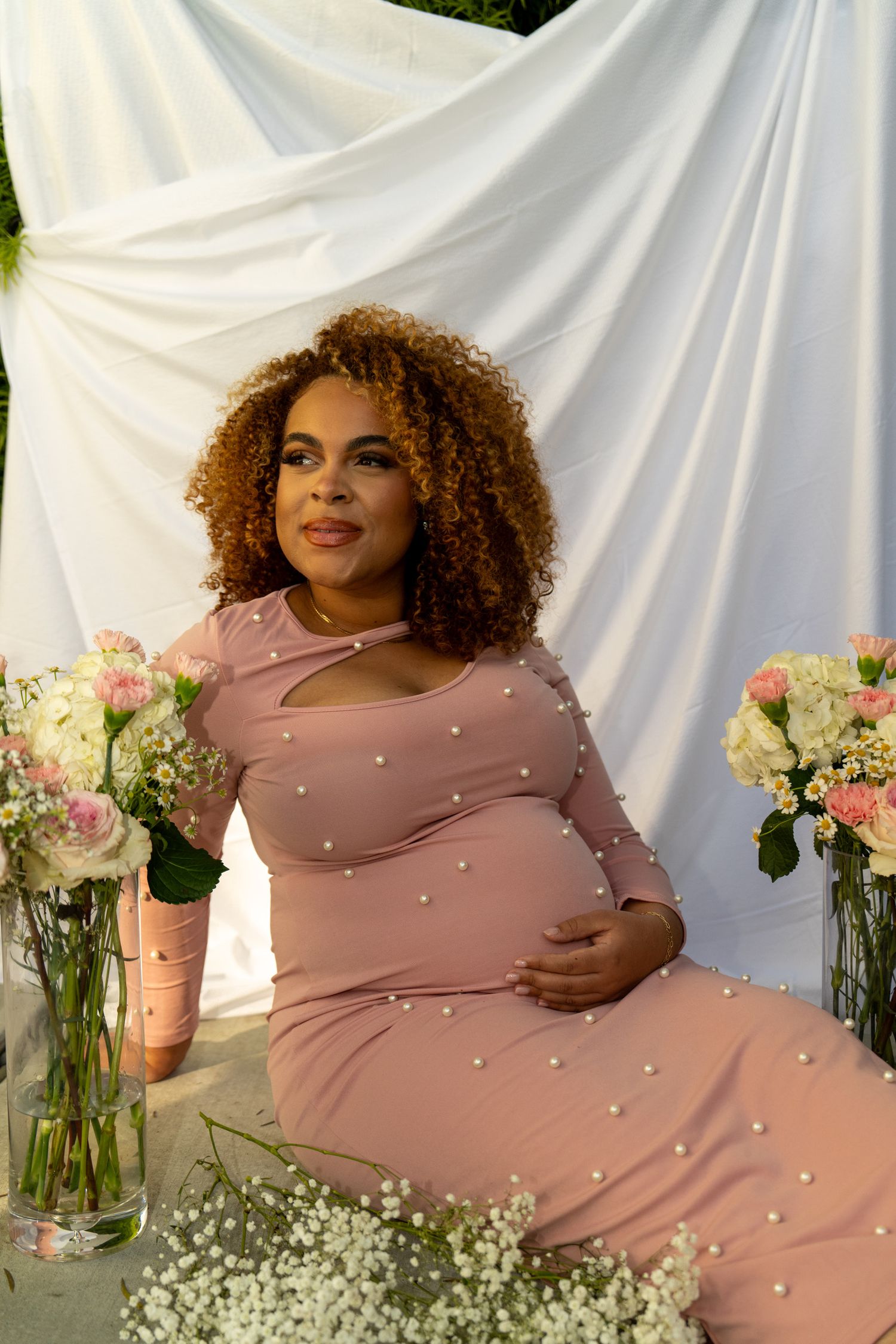 Maternity photoshoot featuring pink pearl dress with white backdrop and floral arrangements.