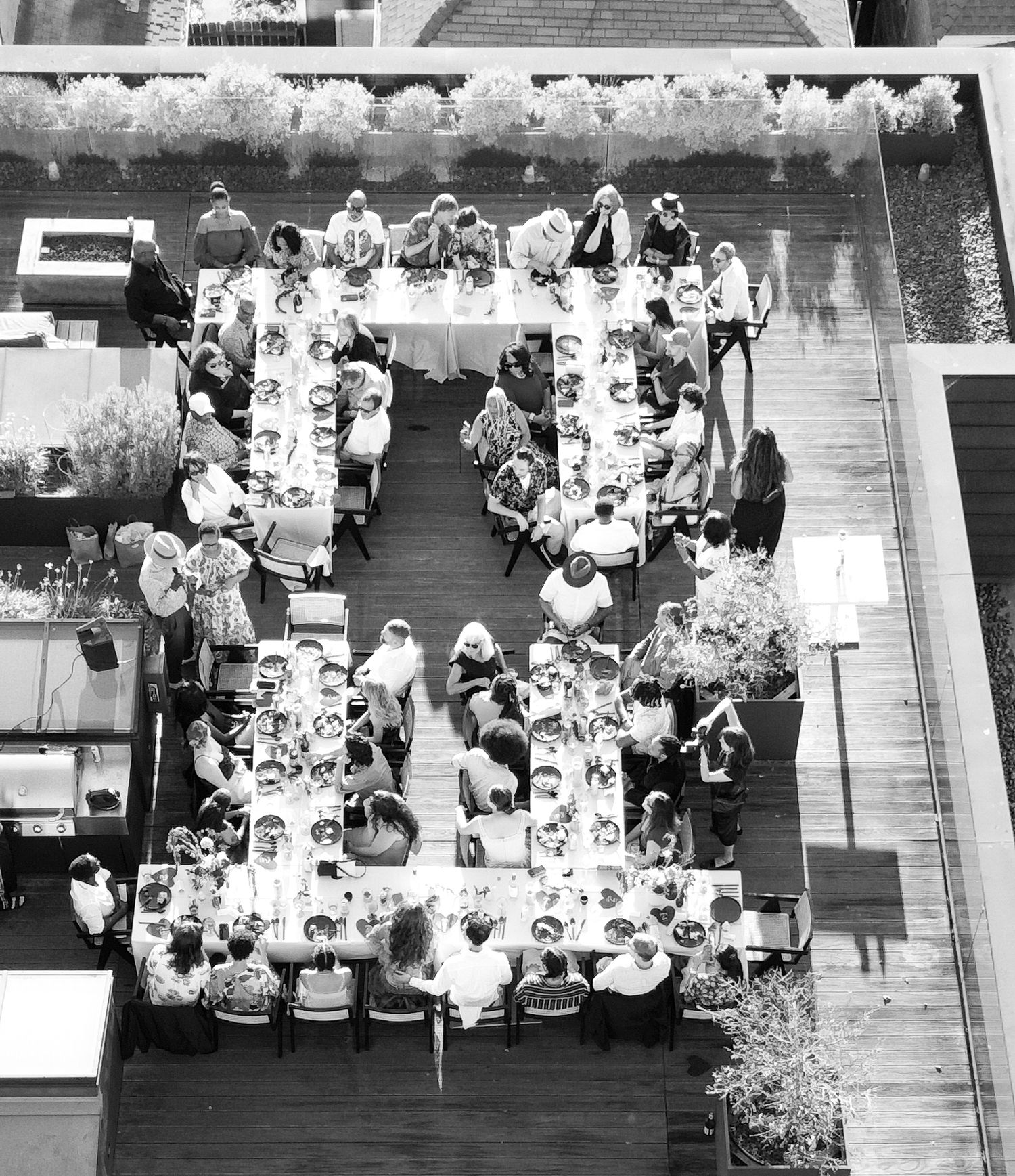 Black and white aerial photograph of guests dining at tables on an outdoor patio.