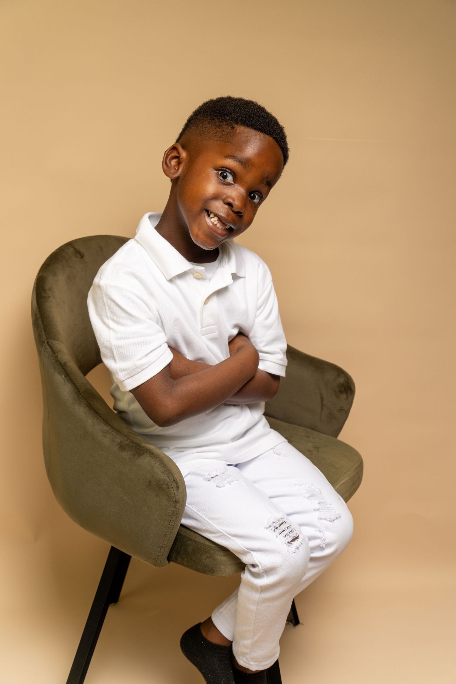 A cozy studio portrait setup with a green velvet chair against a warm beige backdrop.