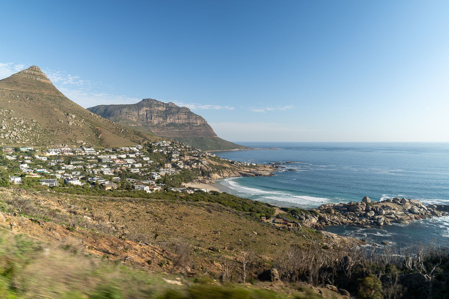 Panoramic coastal view of mountains and beaches along a scenic shoreline under blue skies.