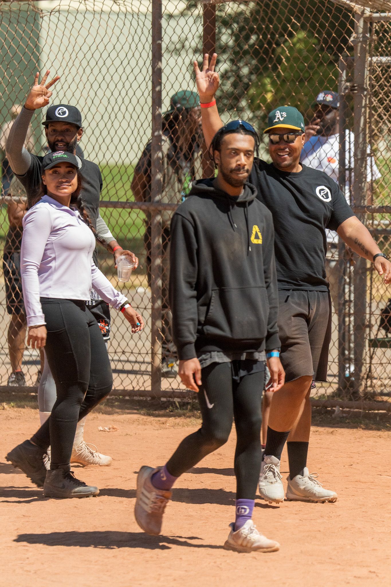 Players and coaches gathered along a chain-link fence at a softball field.