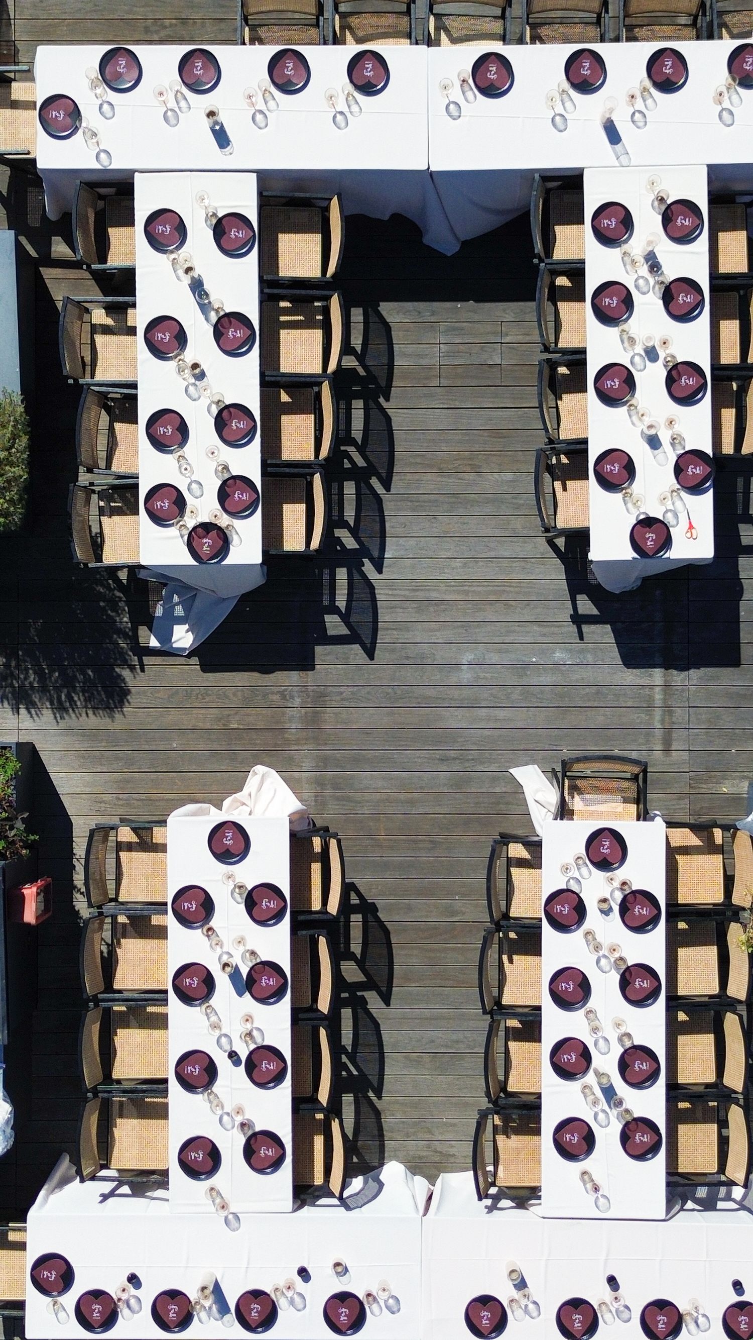 Aerial view of outdoor dining tables arranged with white tablecloths and circular placemats on a wooden deck.