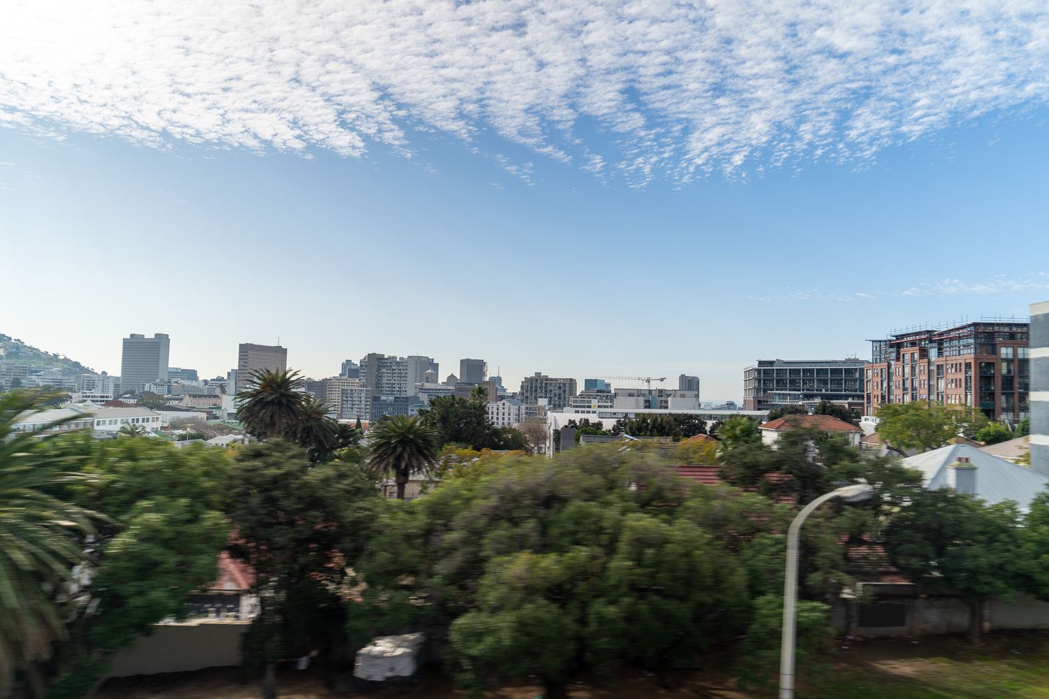 Cityscape view of Cape Town with Table Mountain and scattered clouds above.