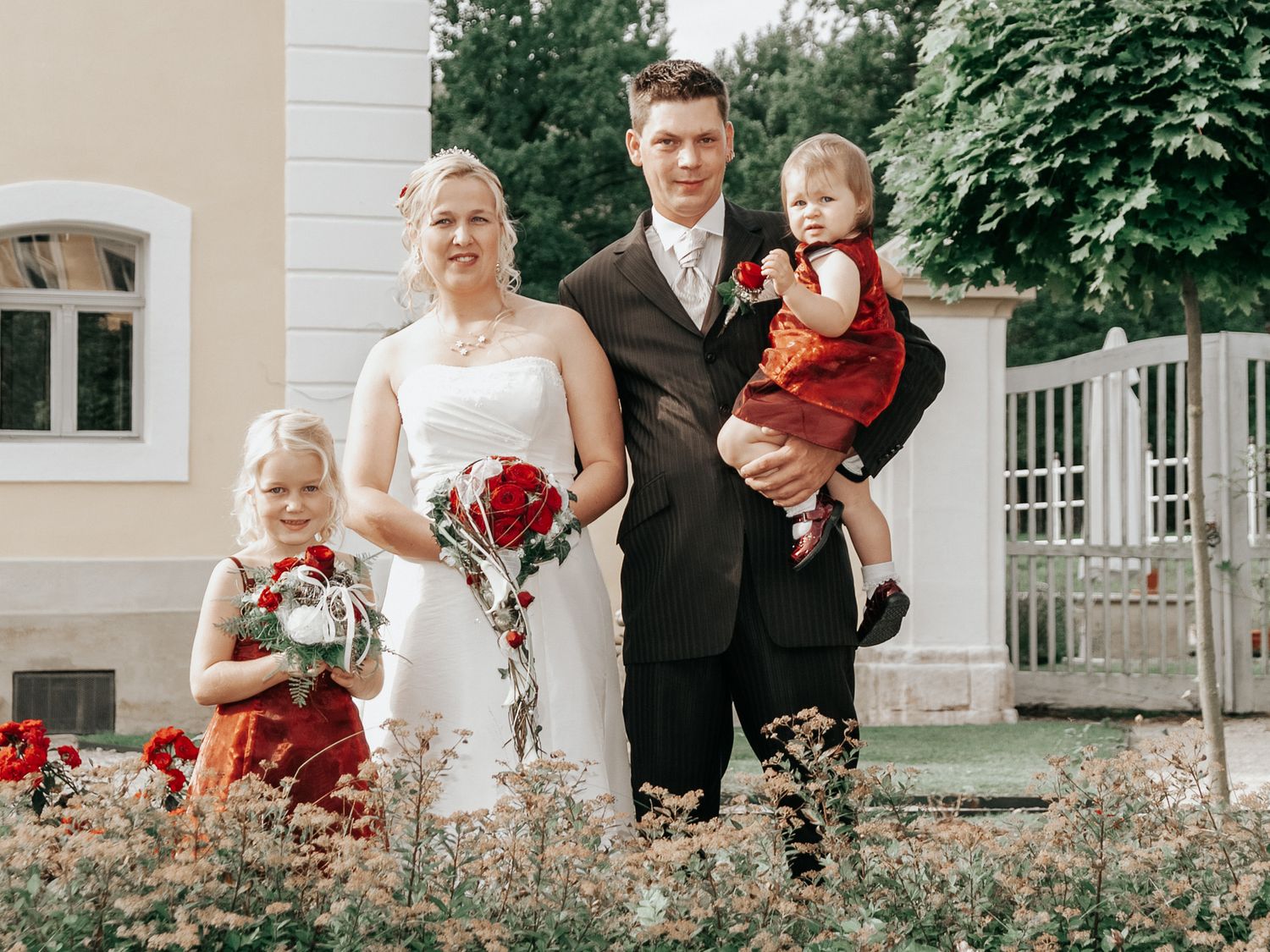 Wedding party poses outdoors on lawn with red and white floral arrangements.