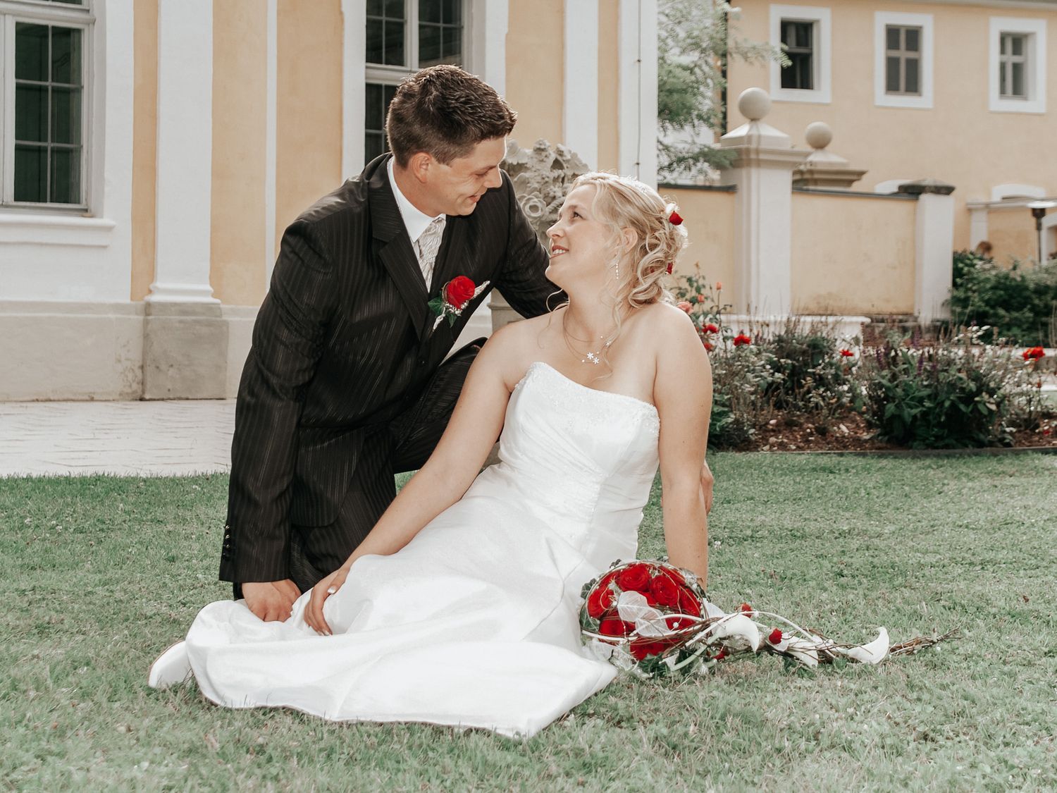 Bride and groom share intimate moment while sitting on grass during outdoor photo session.