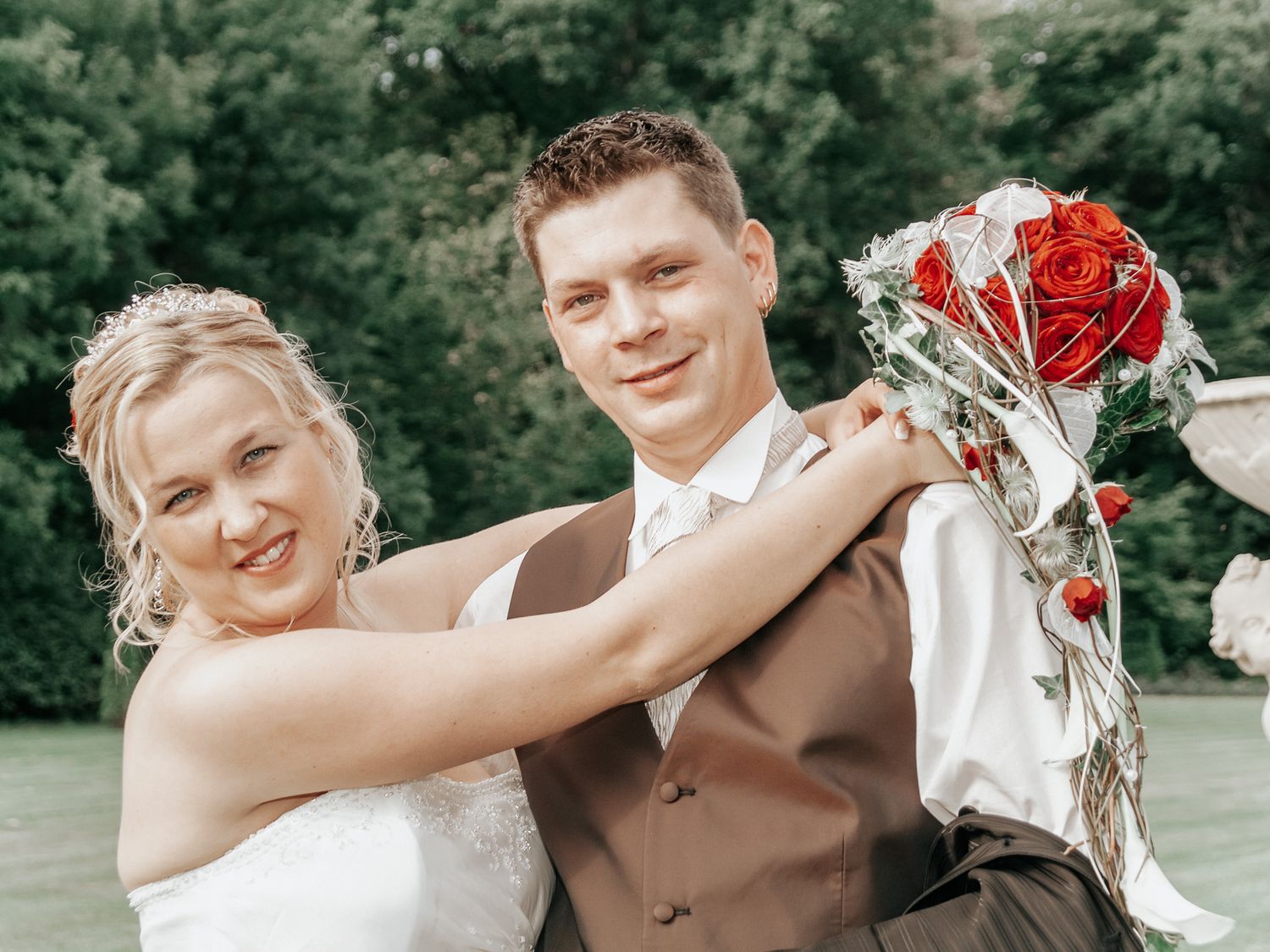 Wedding couple poses in garden setting with romantic red and white floral bouquet.