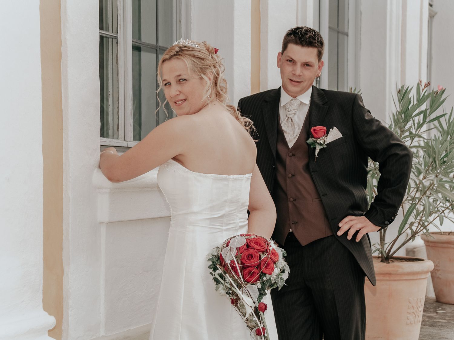 Bride and groom pose together in front of a white building with elegant columns during their wedding photoshoot.