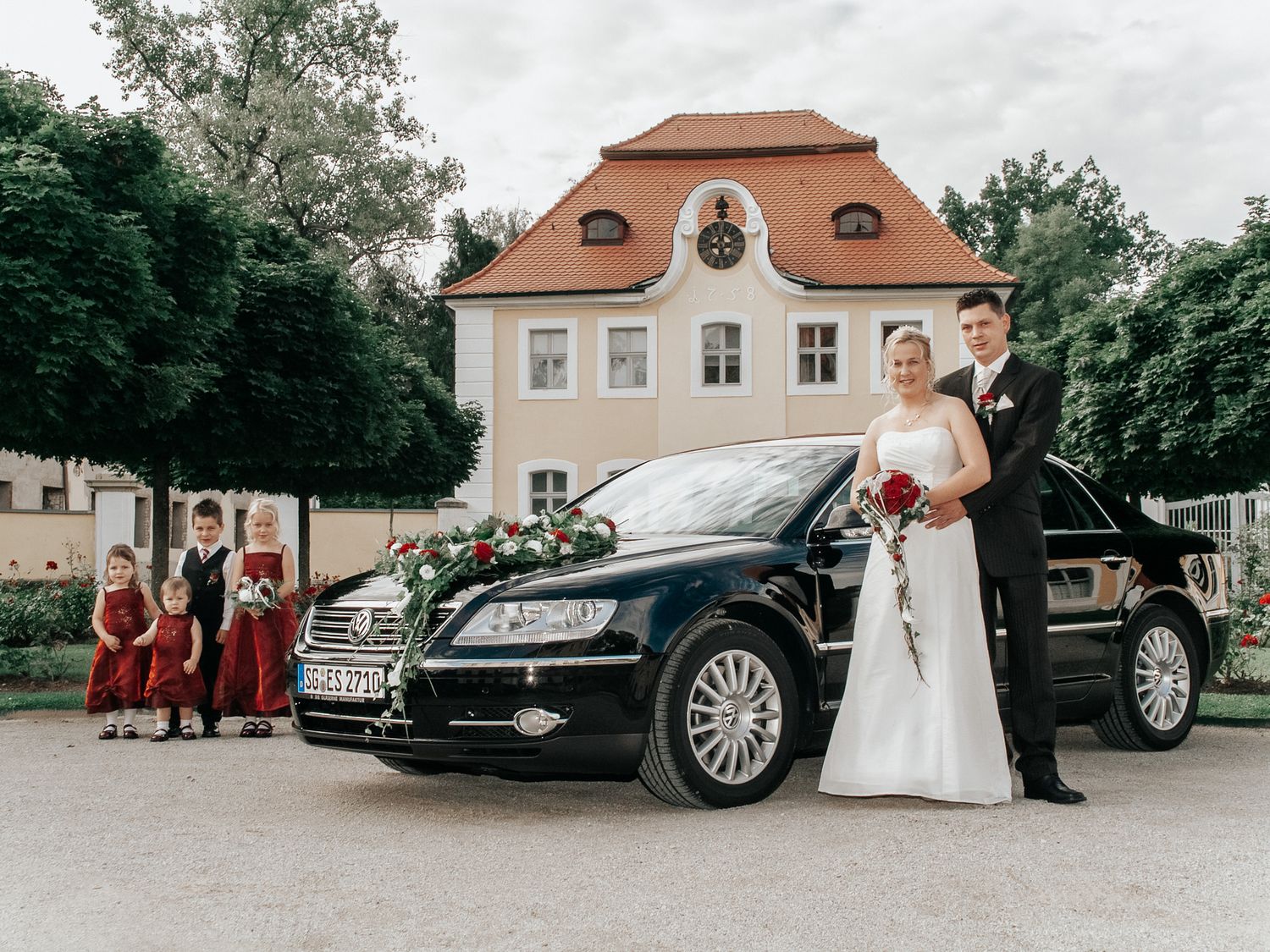 A row of luxury wedding cars parked outside a venue with orange-roofed buildings in the background.