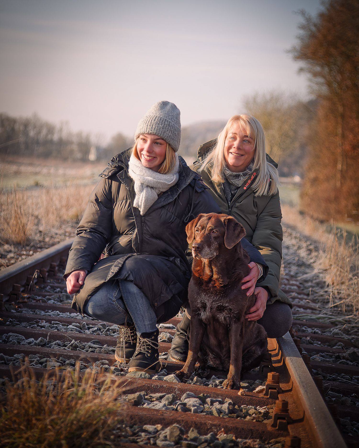 Zwei Menschen und ein brauner Hund entspannen sich zusammen auf Bahngleisen während eines goldenen Herbstsonnenuntergangs. Ort Gasseldorf