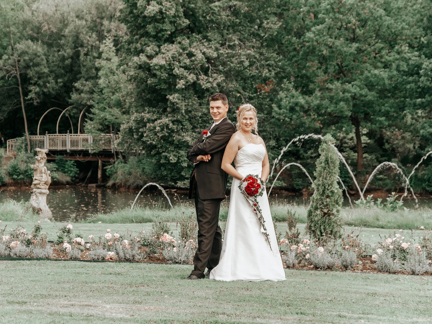 Wedding couple walks hand in hand through a lush garden path with decorative metal arches in the background.