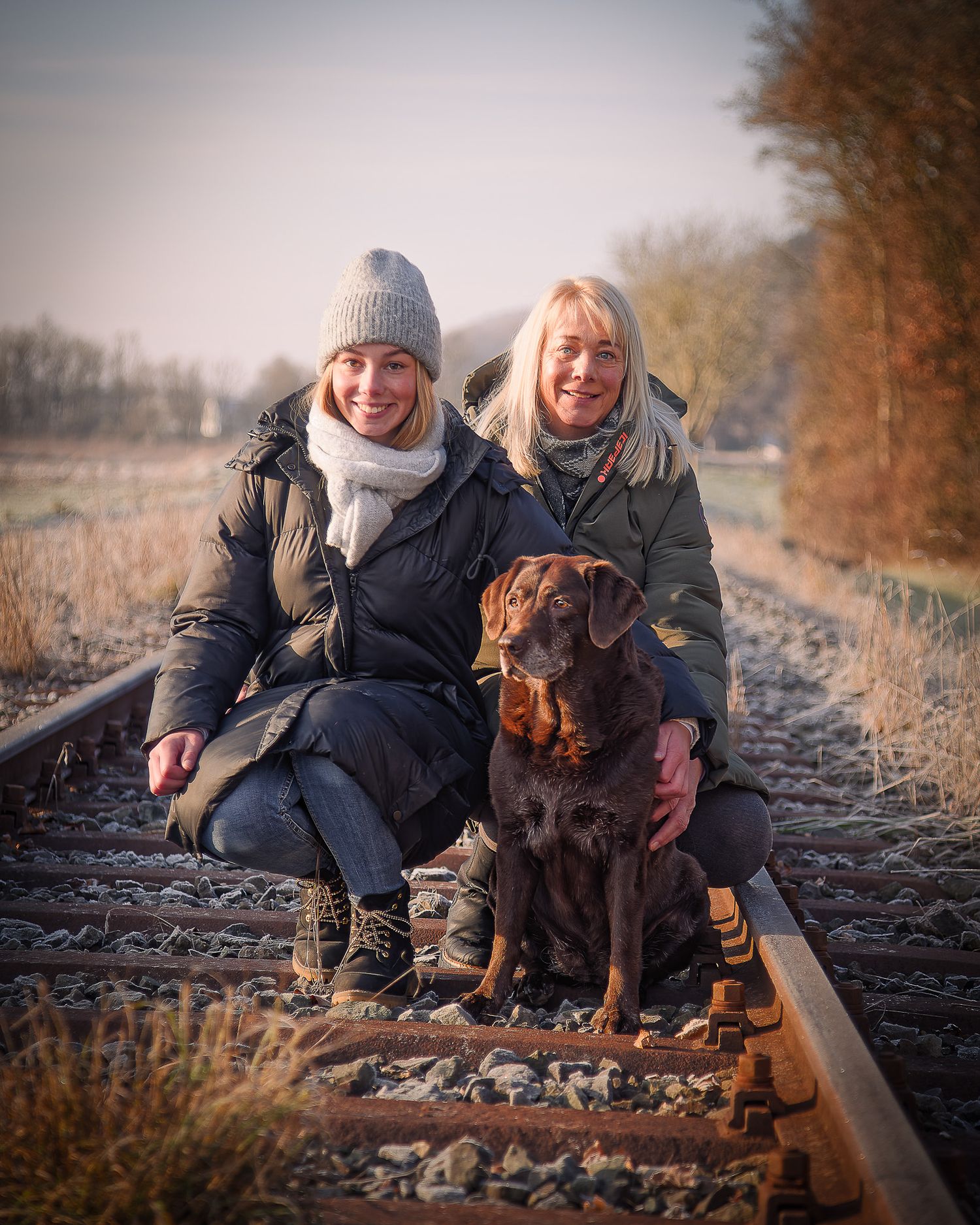 Zwei Menschen und ein Labrador sitzen an einem goldenen Herbstnachmittag zusammen auf Bahngleisen, in Gasseldorf hier fährt die Museumsbahn.