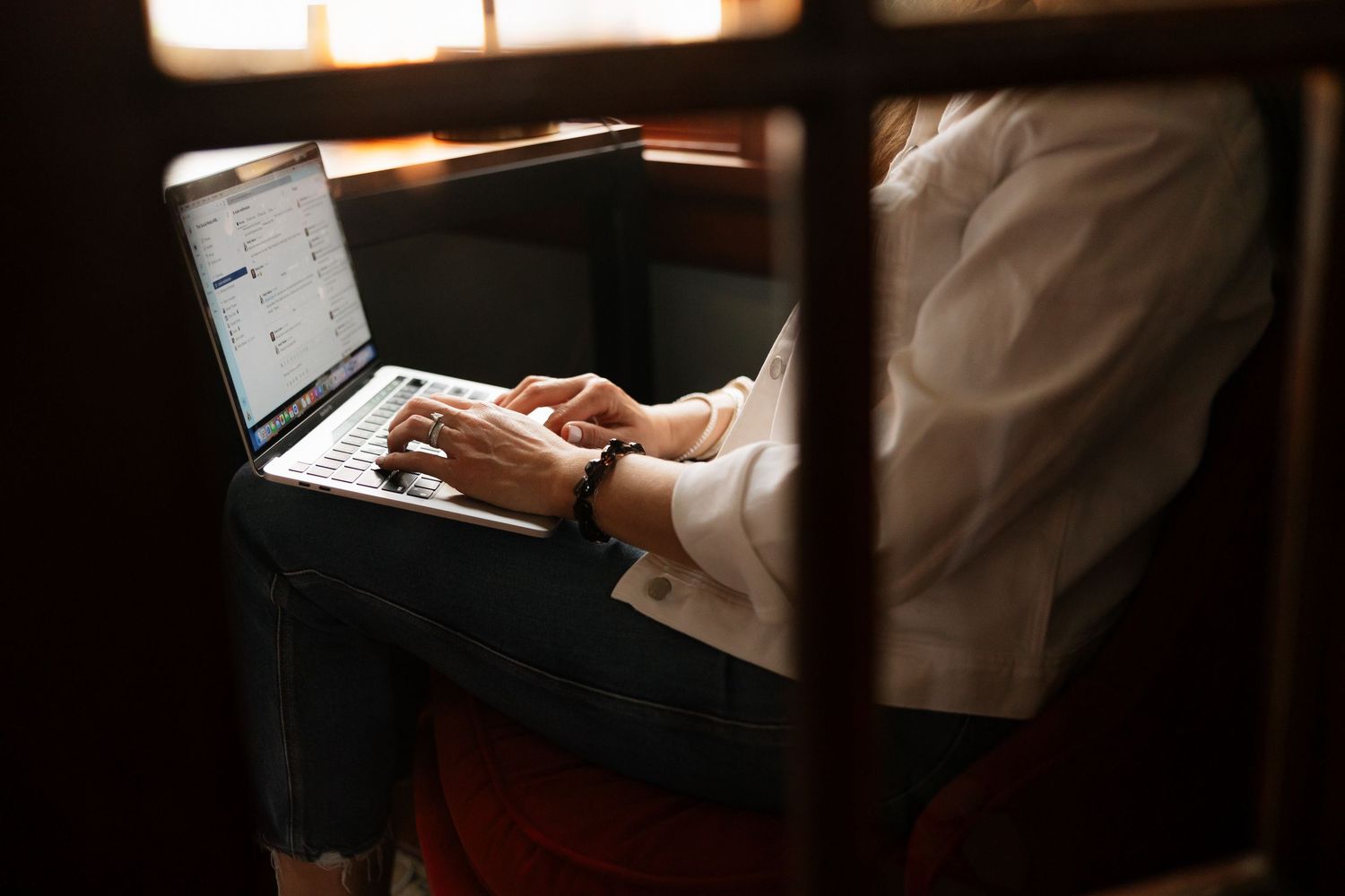 Close-up of hands typing on laptop keyboard, person wearing white shirt and bracelet.