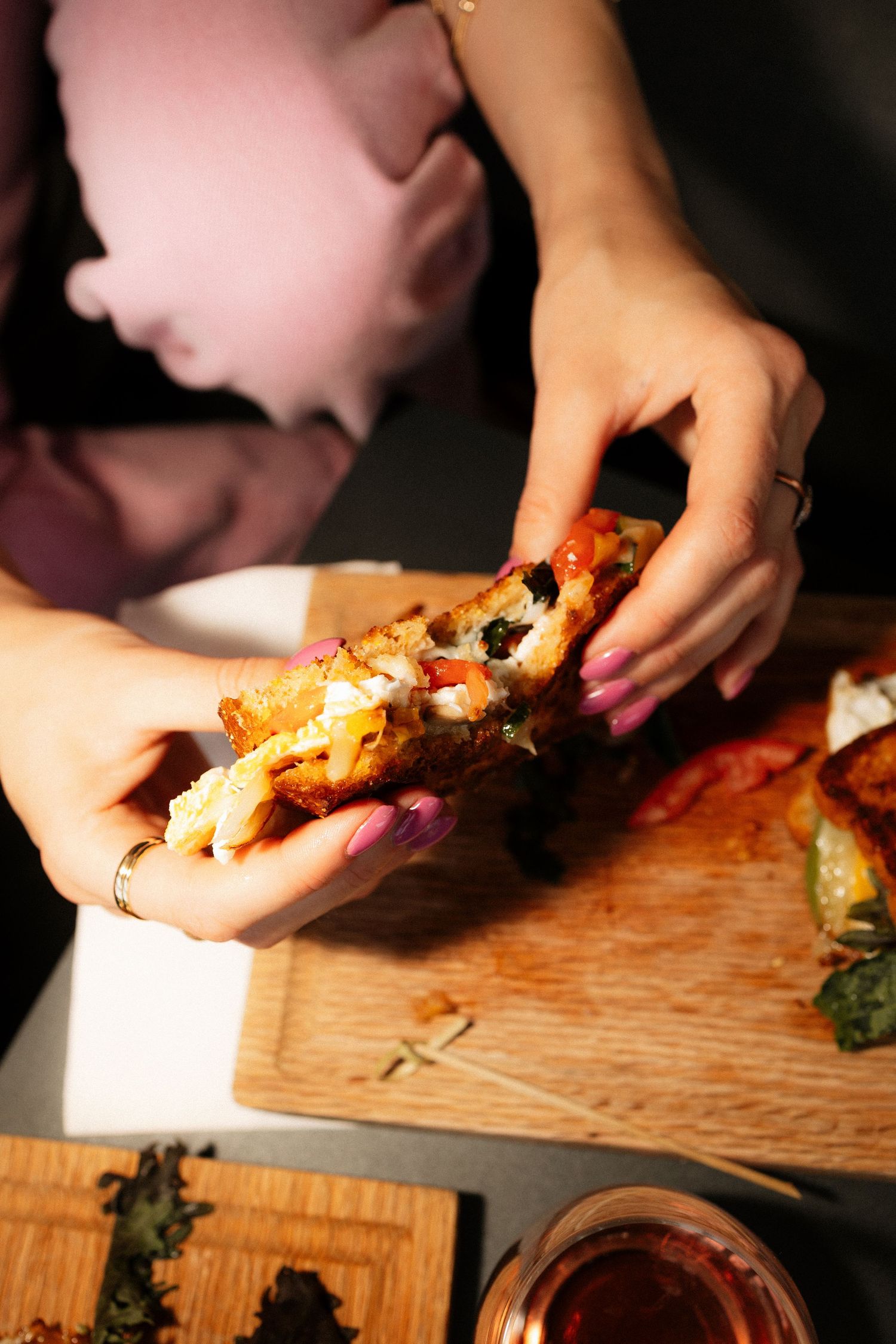 Woman in pink blouse holding a loaded toast with colorful toppings over a wooden cutting board.