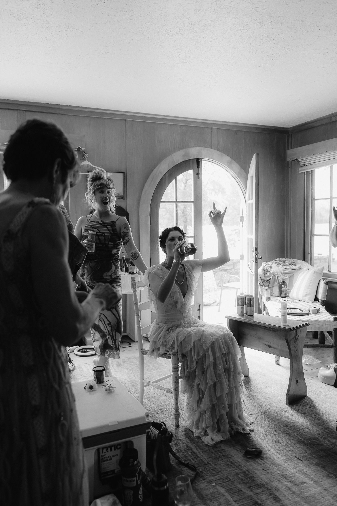 Black and white photo of bridesmaids getting ready, one seated raising a glass in a elegant room.