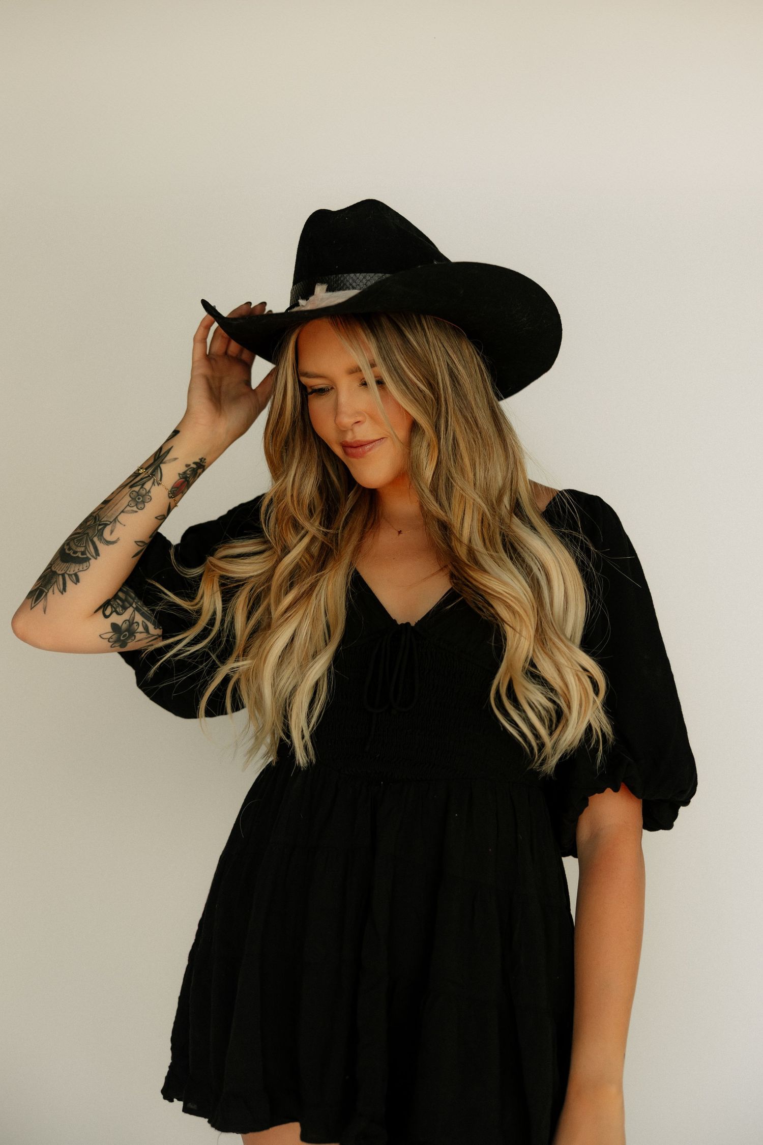 Blonde woman in black cowboy hat and black puff sleeve dress on white background.