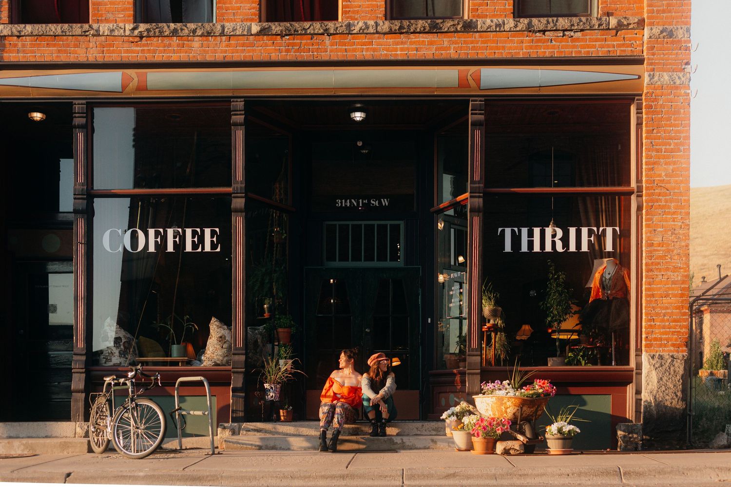 Charming brick storefront with Coffee and Thrift shop signs, couple sitting outside in golden hour light.