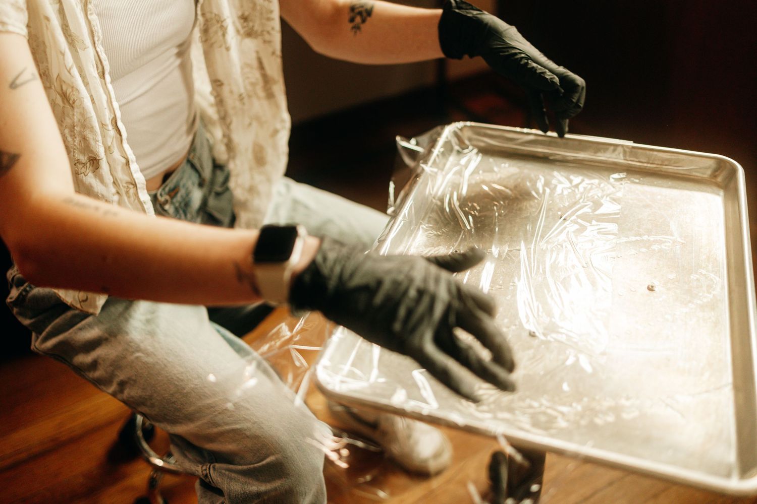 Tattooed artist wearing black gloves holding a metal tray with a printed design during a screen printing process.