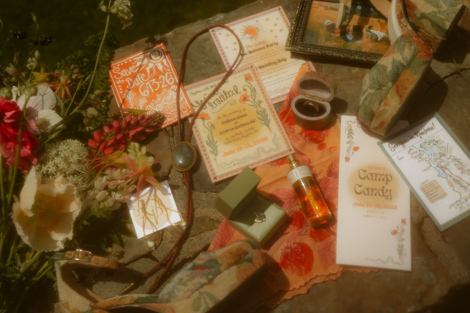 Flat lay of botanical stationery, books, flowers, and amber bottles arranged on a rustic surface.