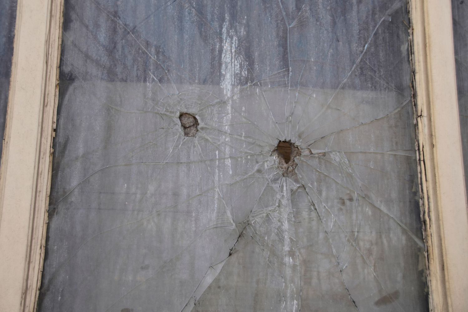 Close-up view of two bullet holes in cracked window glass.