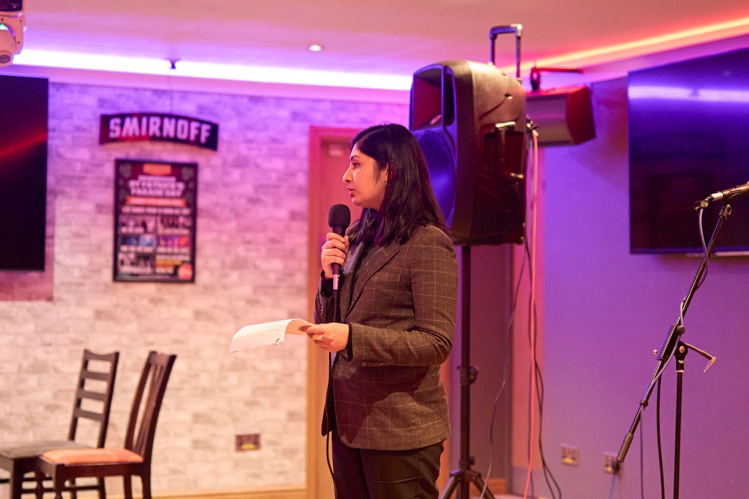 A stand-up comedy performance in a club venue with mood lighting and brick wall backdrop.