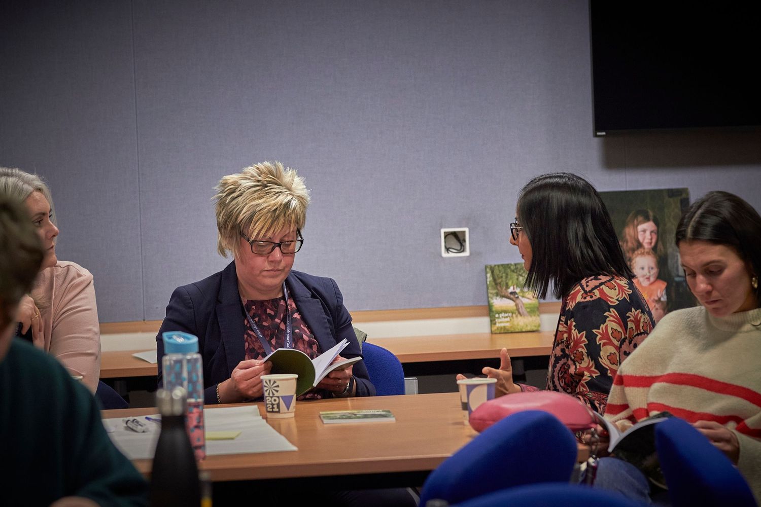 A group of people gathered around a conference table having a discussion over coffee and papers during a meeting.