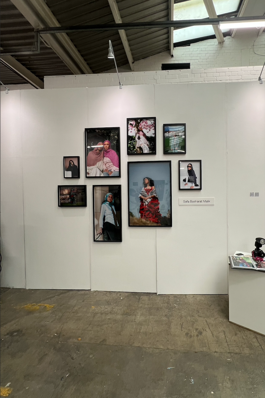 Art gallery wall displaying a curated collection of framed portrait photographs and paintings in an industrial exhibition space.