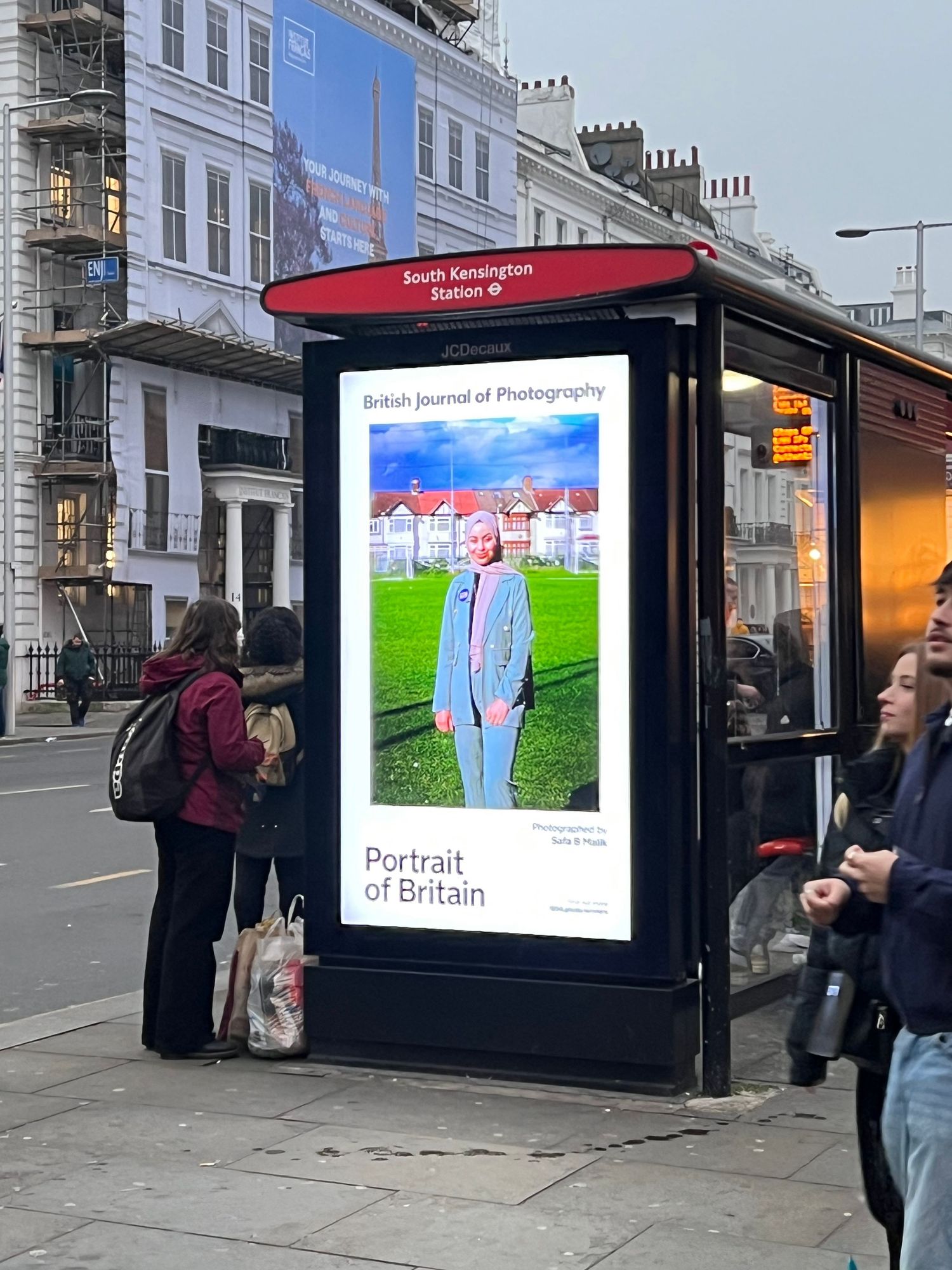 Digital billboards displaying Portrait of Britain exhibition along a city sidewalk.