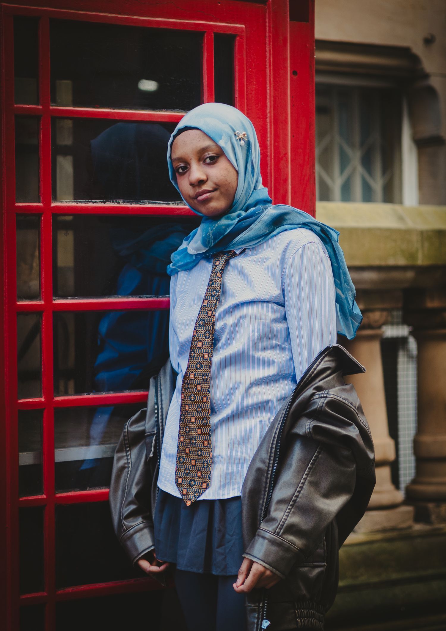 Street style photography next to red phone booths showing modern modest fashion.