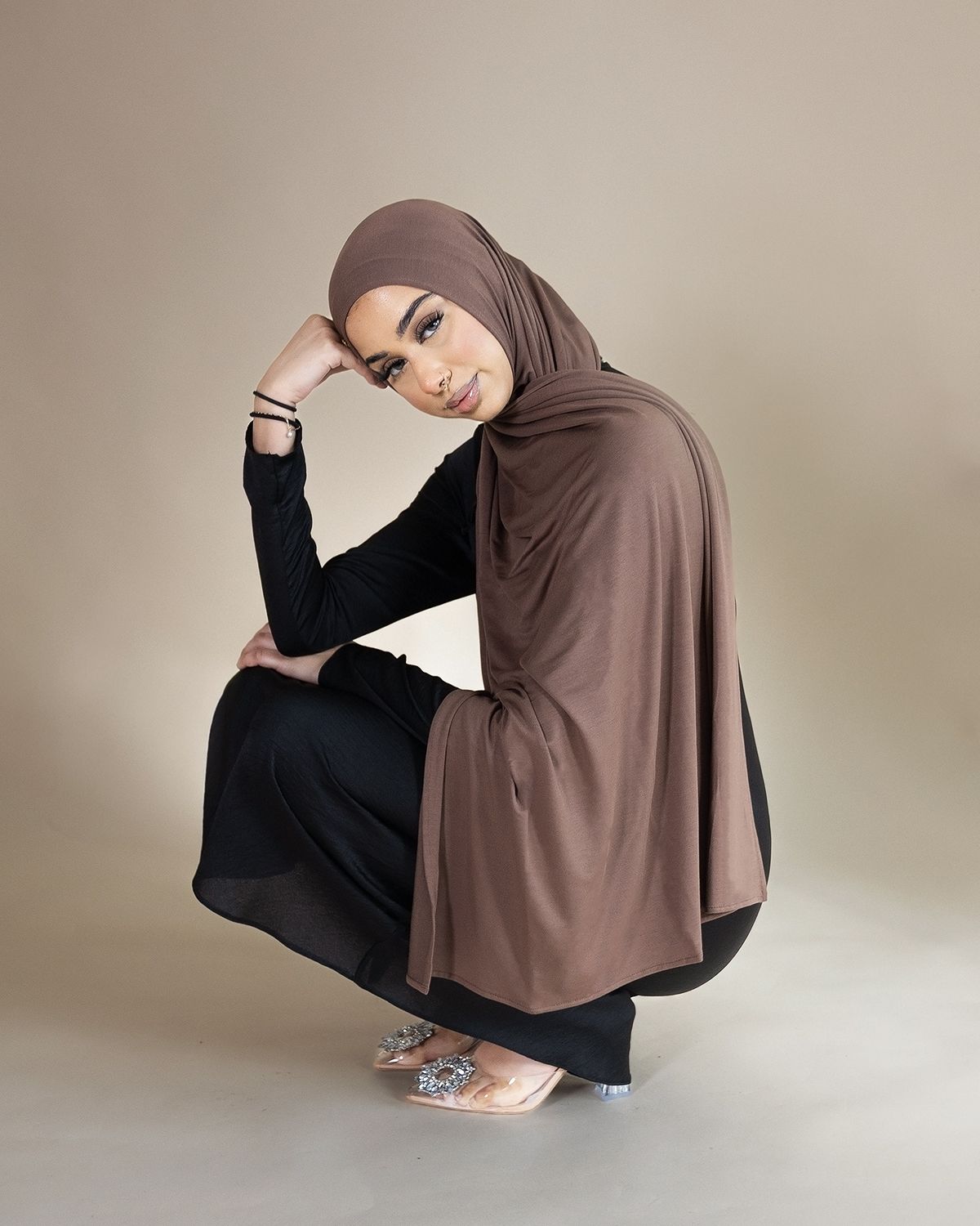 A sequence of fashion photos showing a model in brown hijab and black dress posing gracefully against a neutral backdrop.