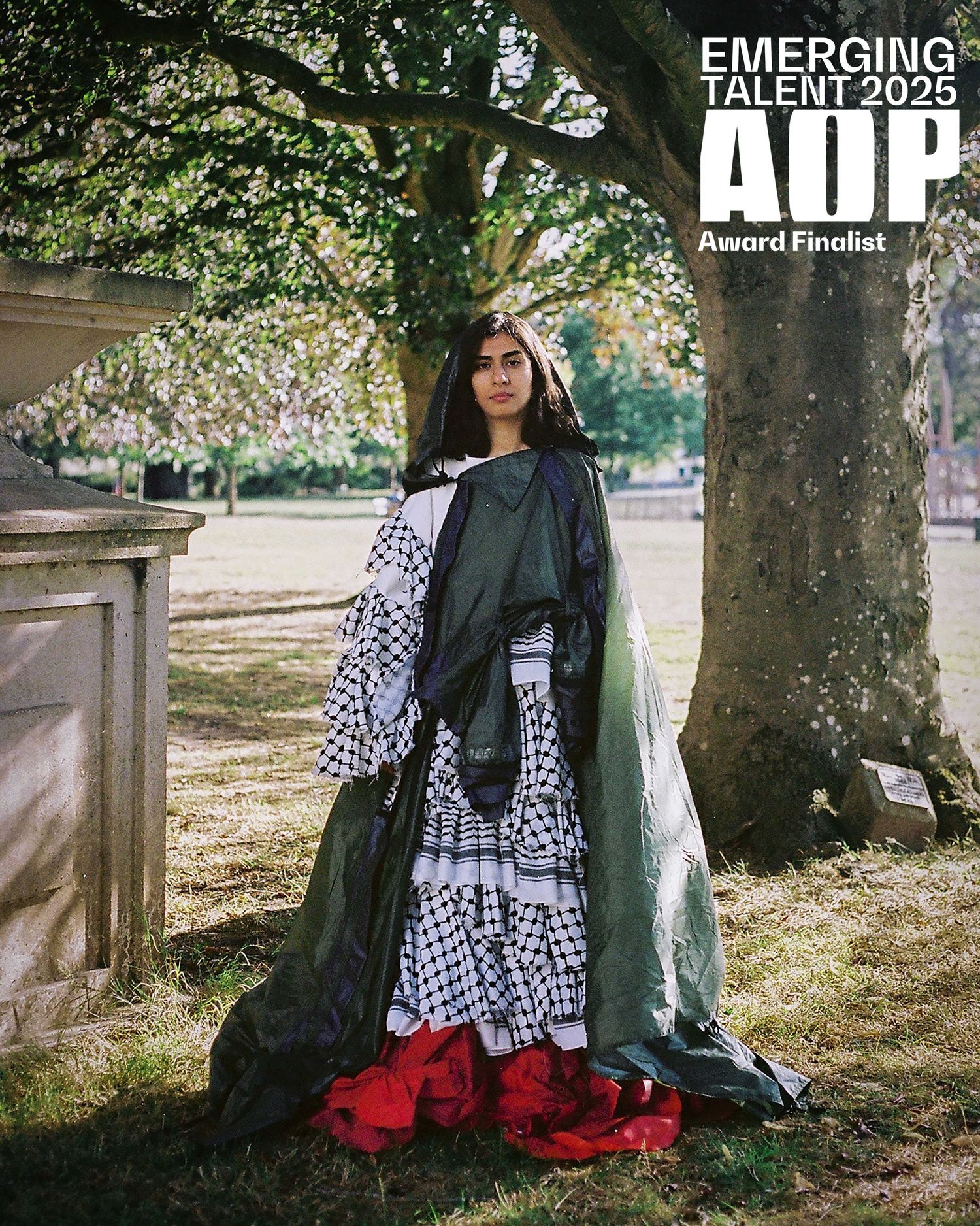 Woman in layered keffiyeh and green fabric gown poses outdoors near tree, AOP Emerging Talent 2025 Award Finalist.