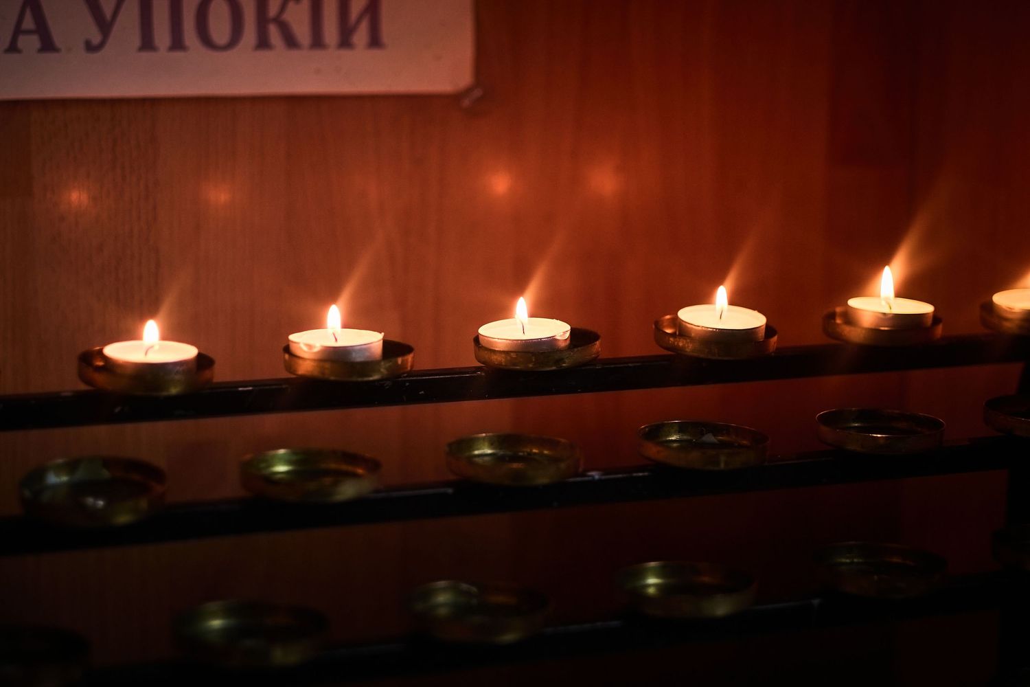 Line of tea light candles burning on a dark wooden shelf.