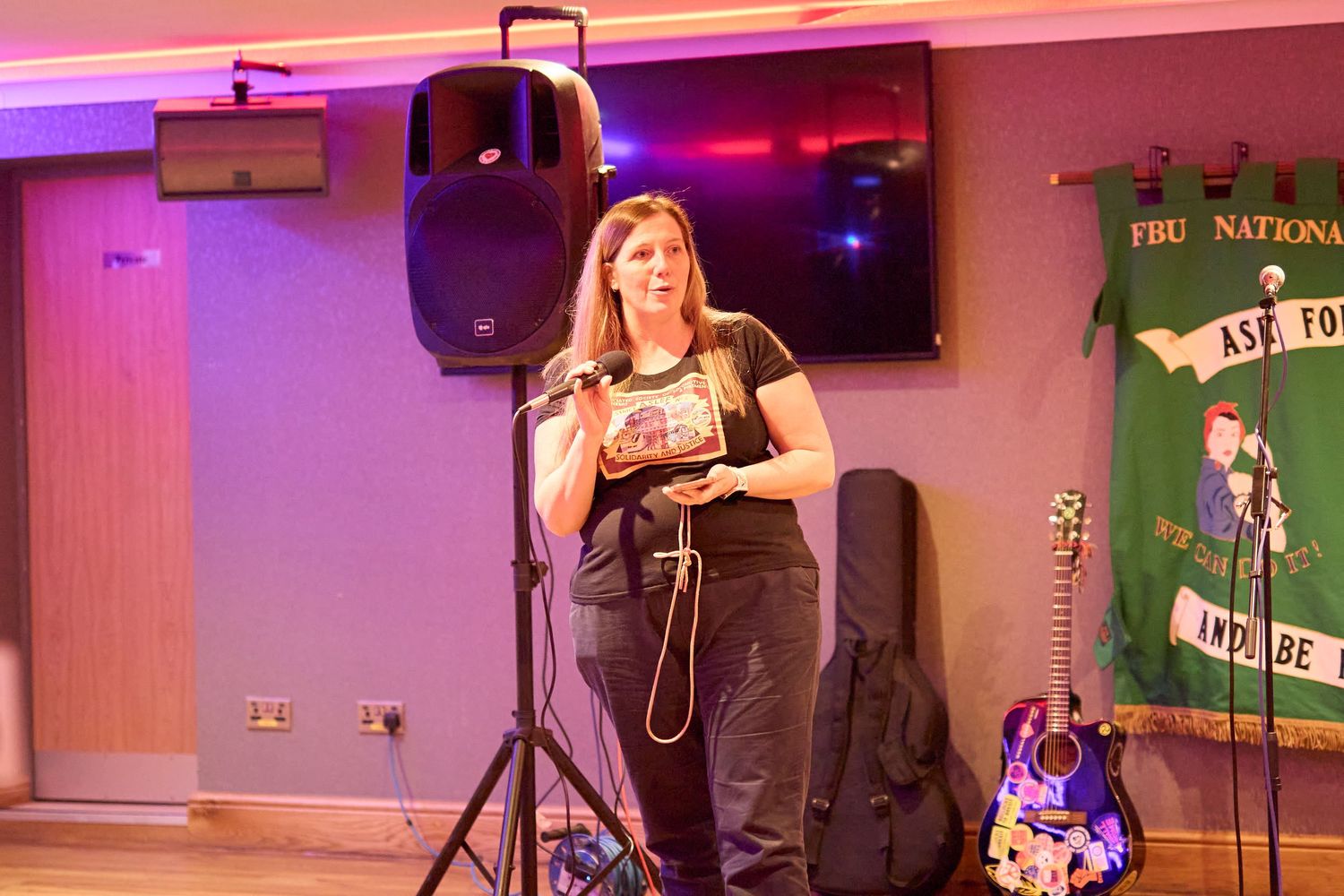 Musicians perform on stage in a venue with purple lighting and green banners visible in the background.